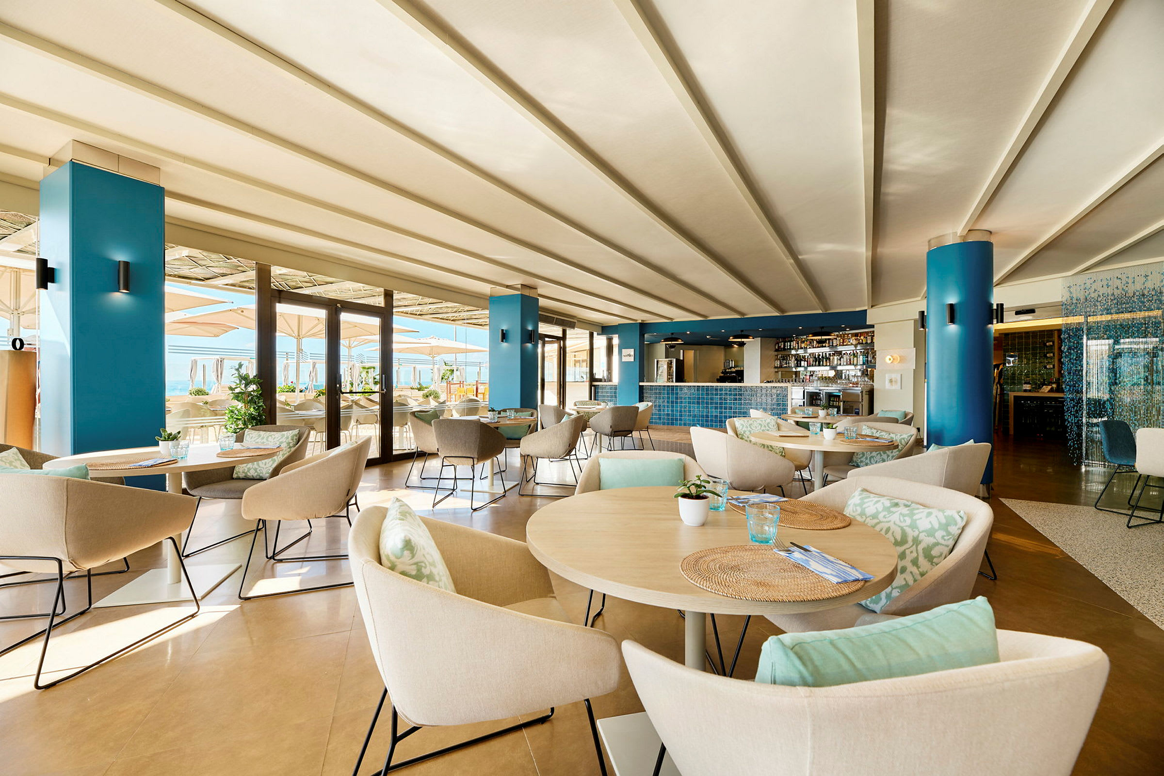 En moderne restaurant med bord og stoler, innredet i lyse farger og med utsikt mot en terrasse. (AI-generert tekst)