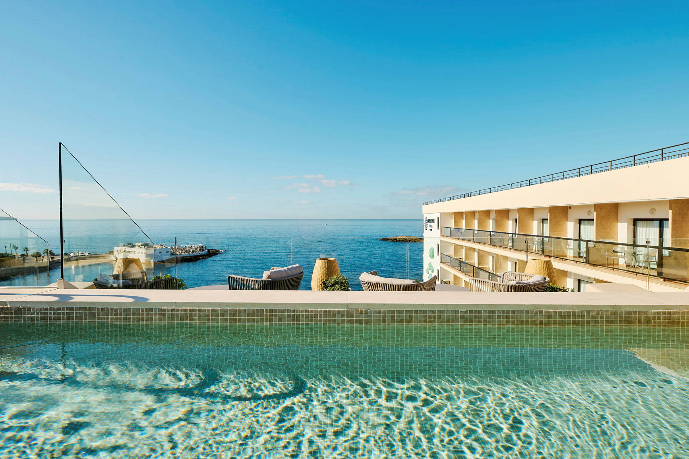 Utendørs svømmebasseng med utsikt mot havet og en hotellbygning. (AI-generert tekst)