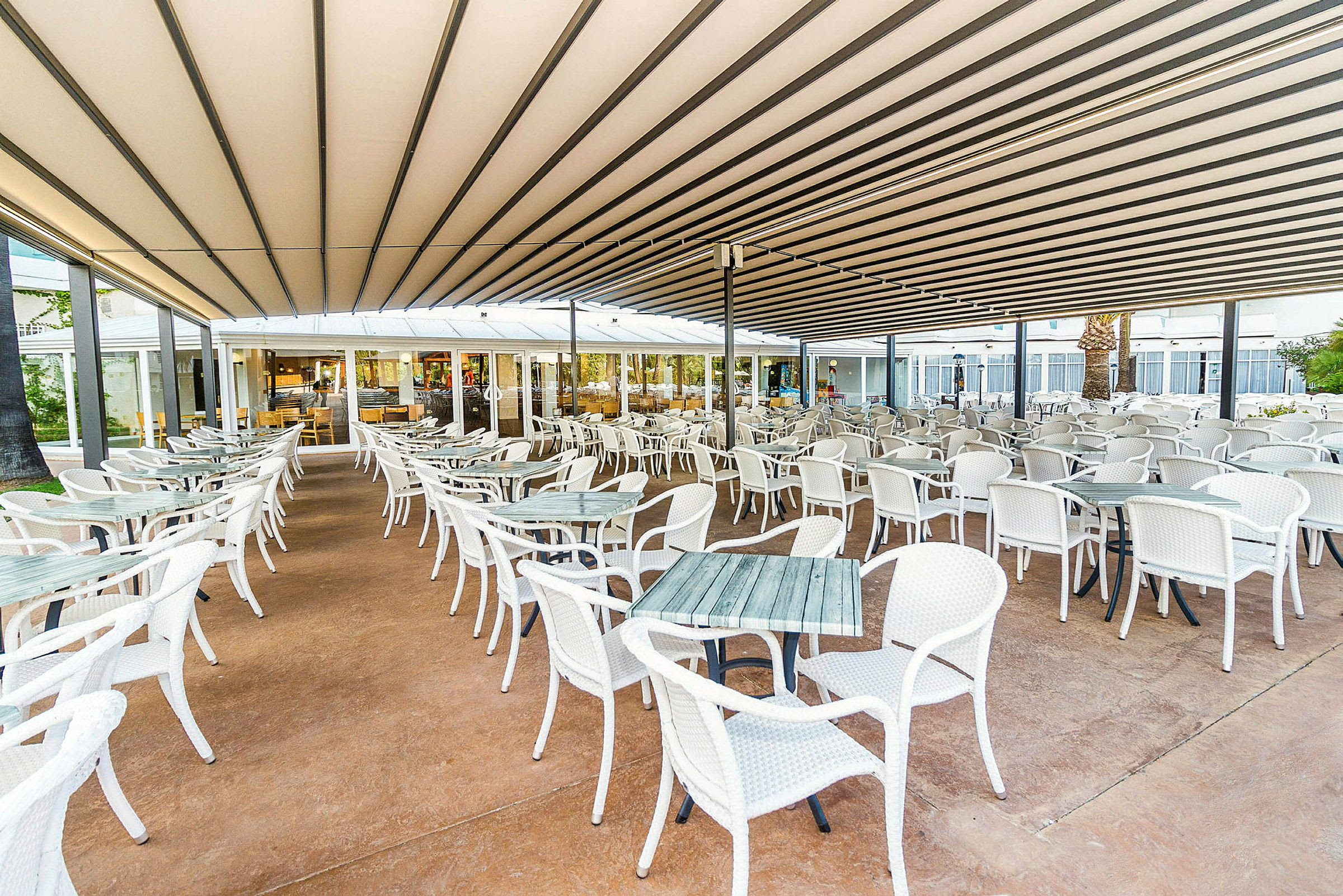 En utendørs restaurant med mange hvite bord og stoler under et tak. (AI-generert tekst)