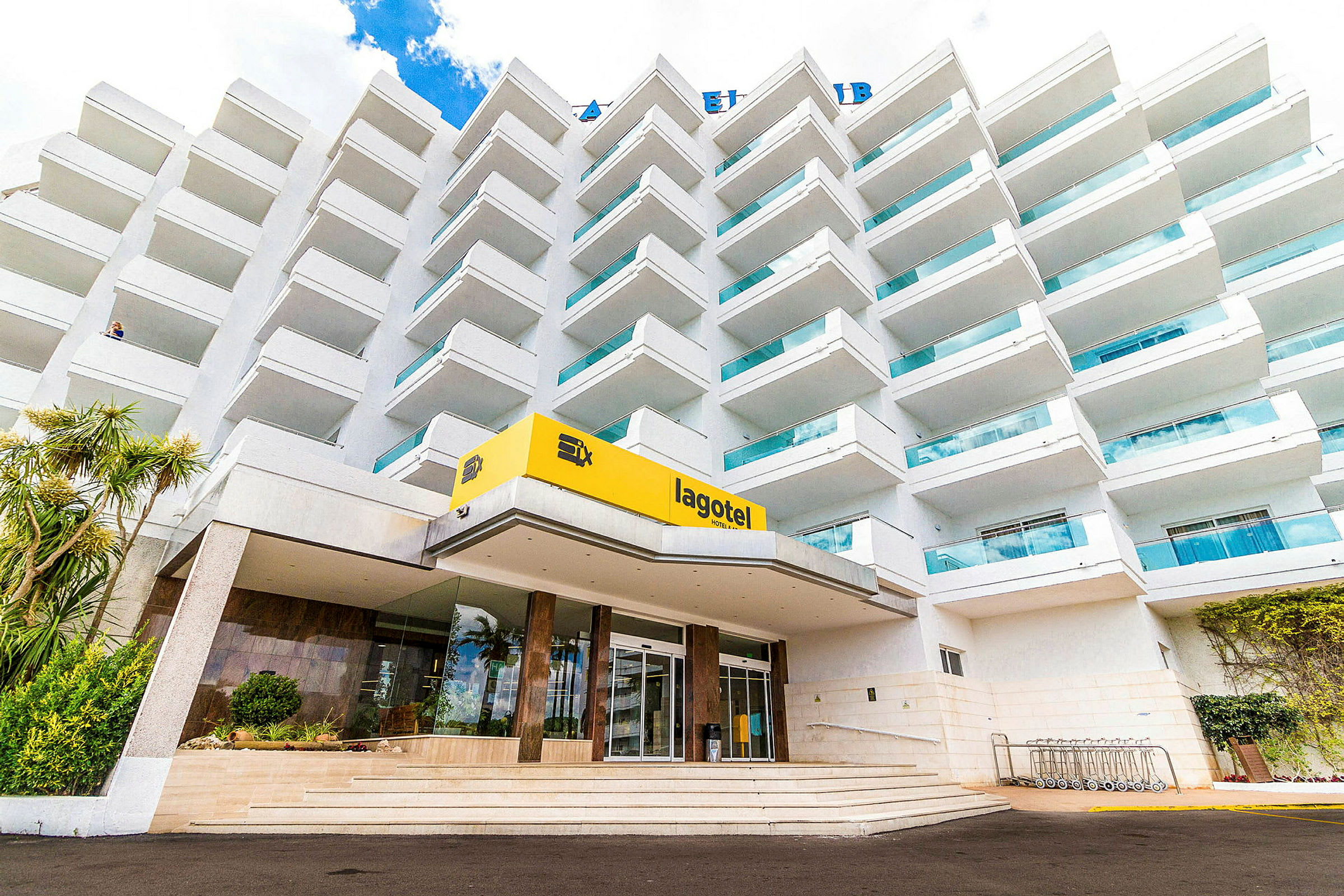 Et fleretasjes hotell med balkonger og en inngang med et gult skilt der det står 'lagotel'. (AI-generert tekst)