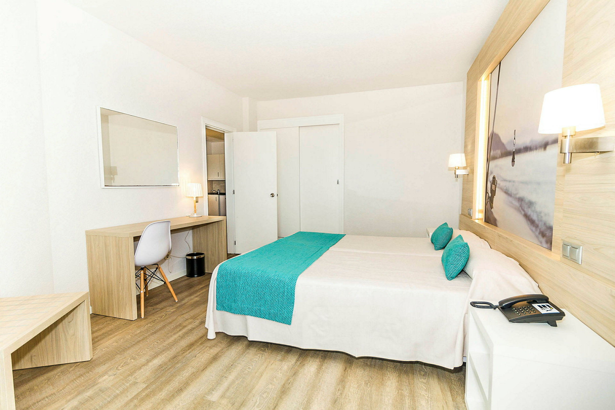 Et hotellrom med en dobbeltseng, tremøbler og en arbeidsplass med en stol og en lampe. (AI-generert tekst)