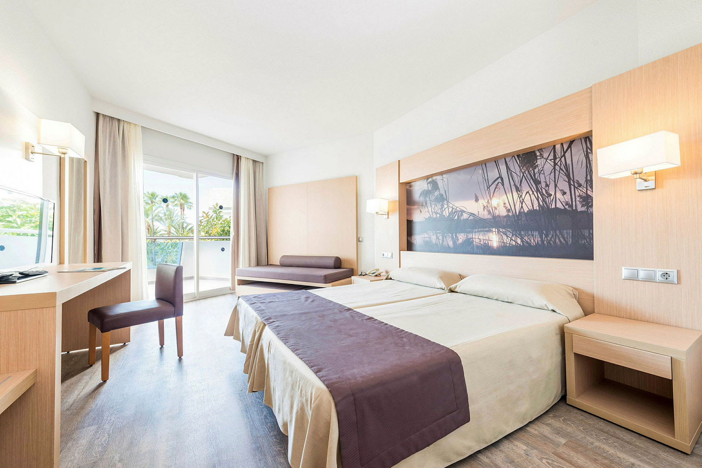 Et hotellrom med en dobbeltseng, skrivebord, stol og en sofa. Rommet har en glassdør som fører til en balkong. (AI-generert tekst)