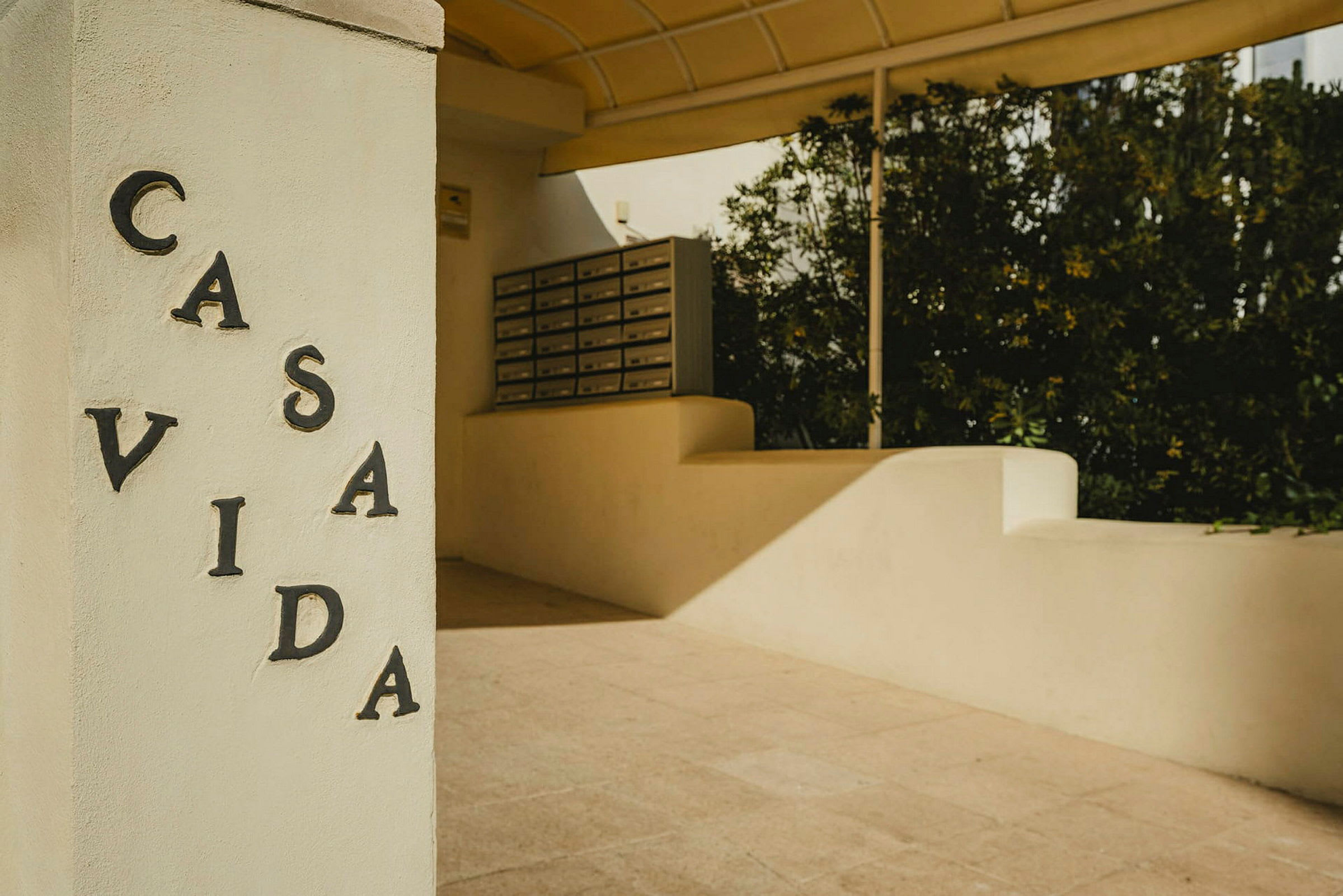 Et hvitt steinfundament med teksten "CASA VIDA" og postkasser i bakgrunnen. (AI-generert tekst)