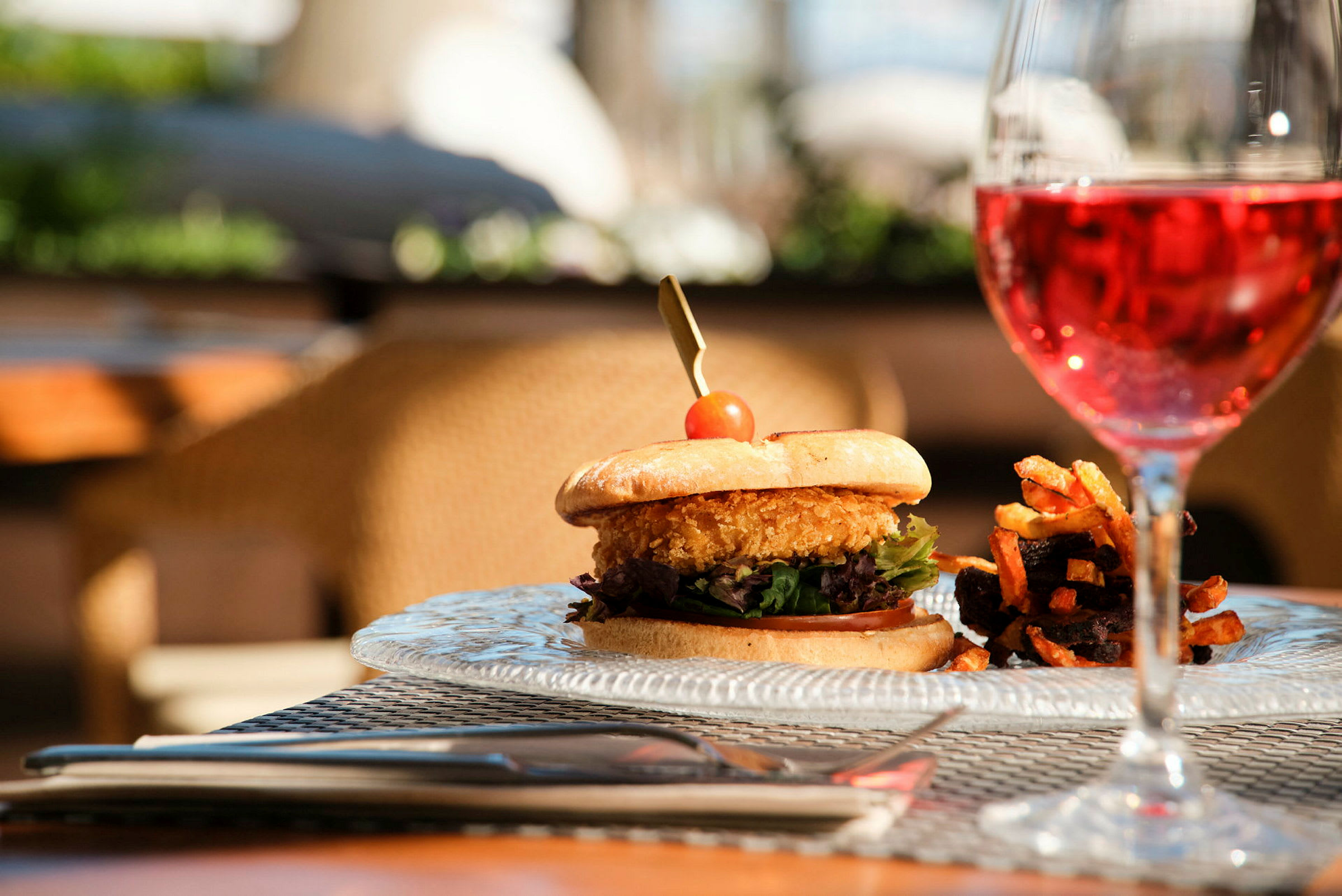 En tallerken med en hamburger ved siden av pommes frites og et glass rosévin. (AI-generert tekst)