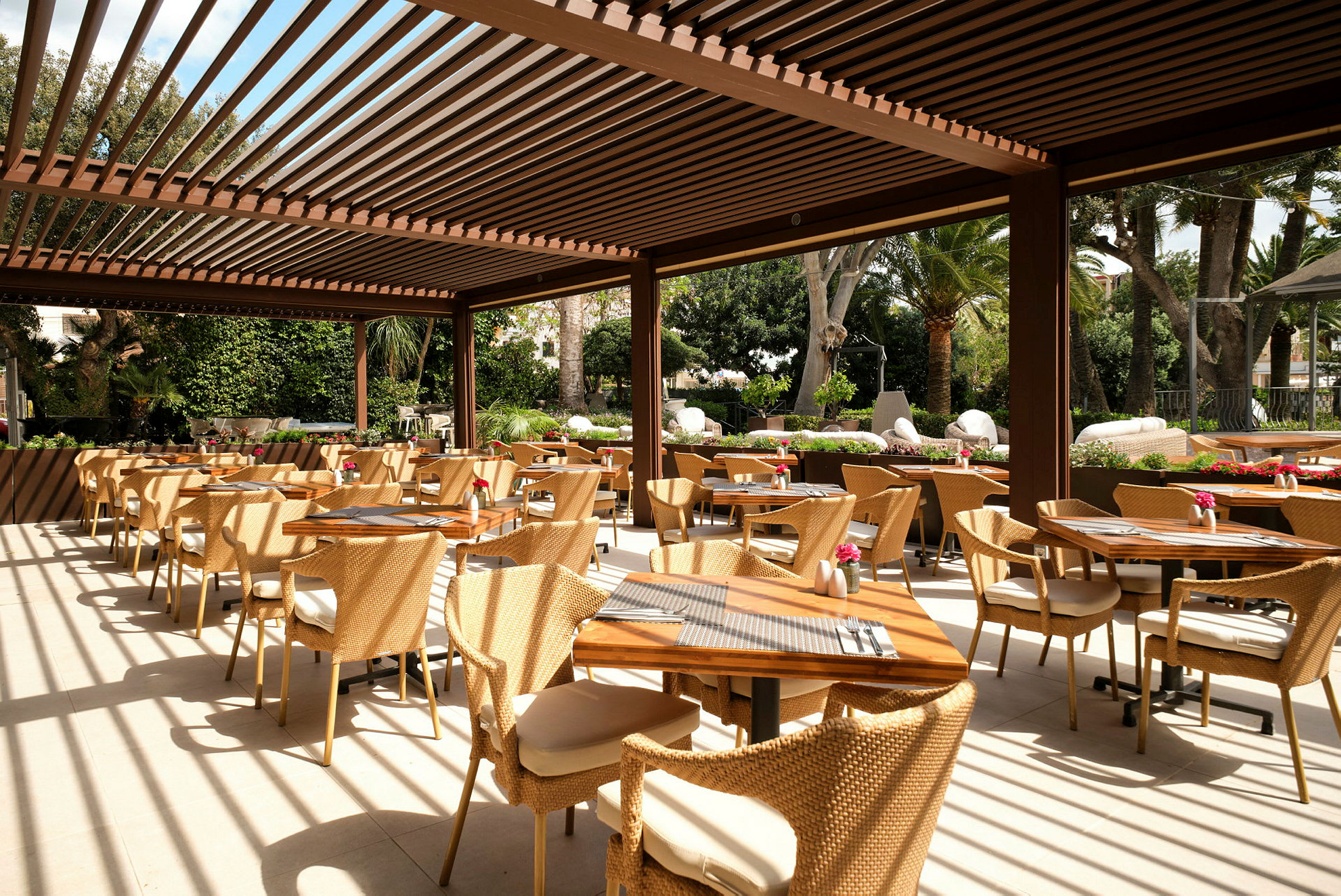 En utendørsrestaurant med bord og stoler og pergola. (AI-generert tekst)