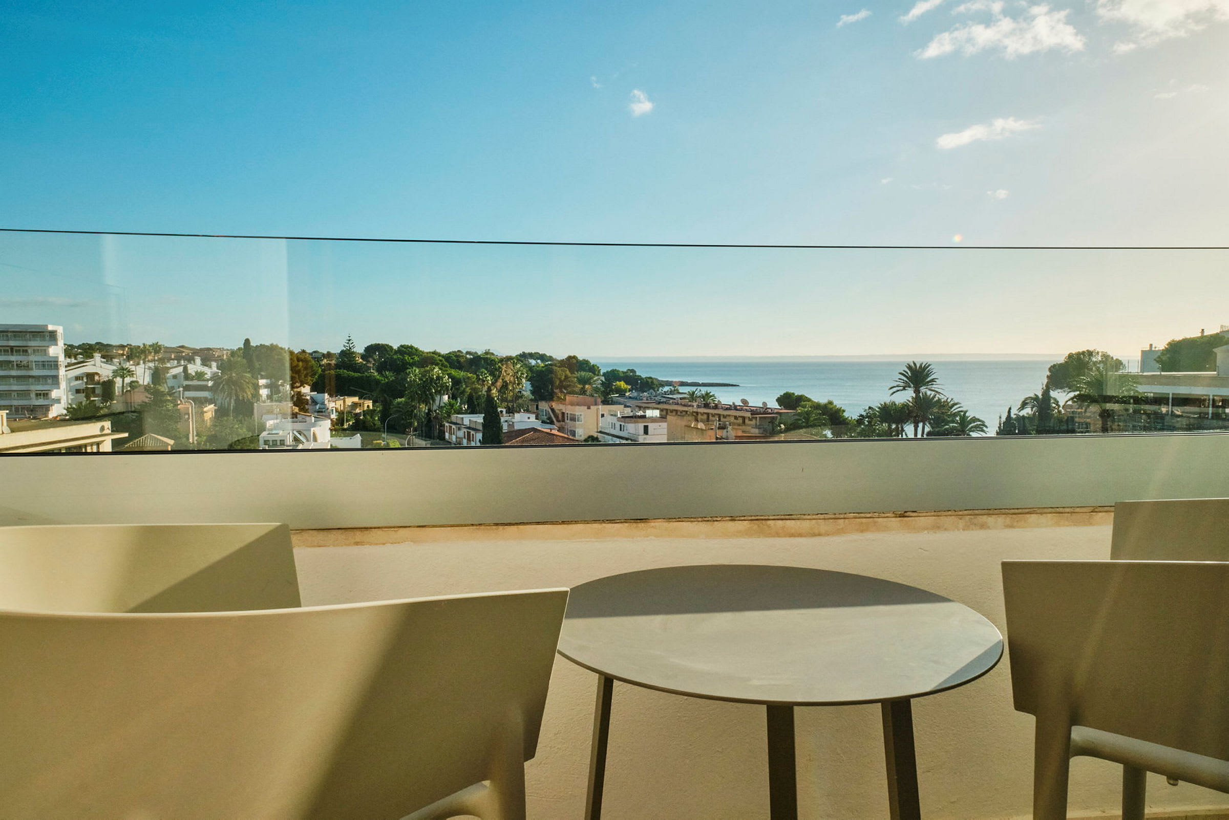 Utsikt fra en terrasse med bord og stoler, med en utsikt over en by og havet i bakgrunnen. (AI-generert tekst)