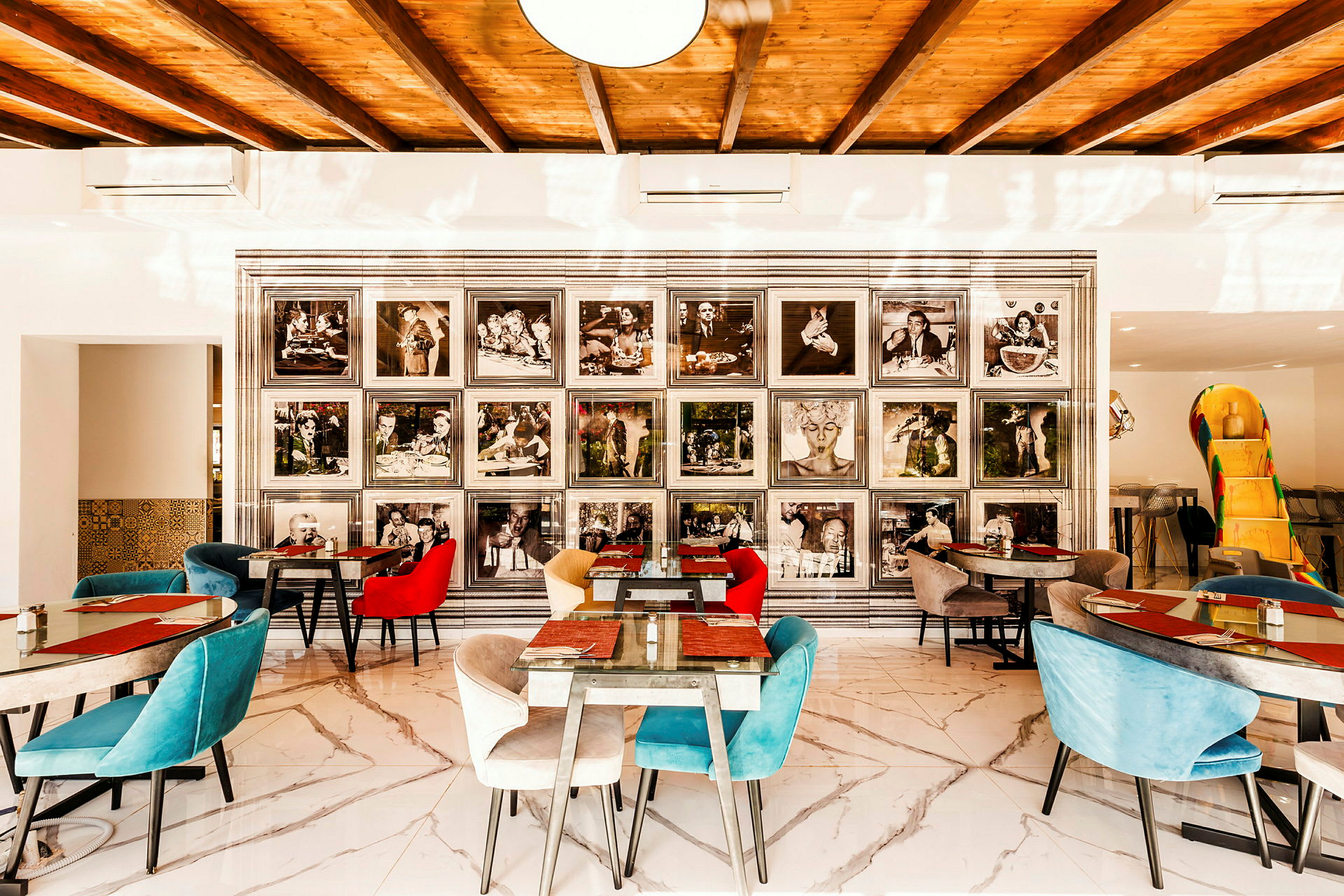 En restaurantinteriør med fargerike stoler og marmorfliser. På veggen vises svart-hvite fotografier i rammer. (AI-generert tekst)