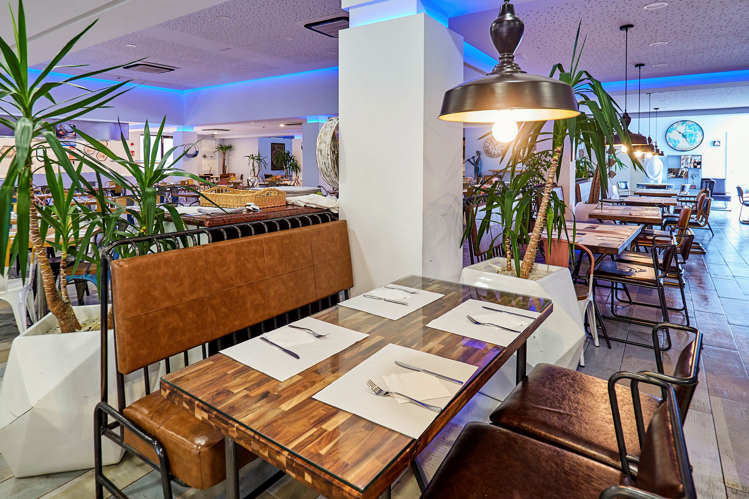 En restaurantinteriør med bord og stoler, dekorert med innendørs planter og belysning. (AI-generert tekst)