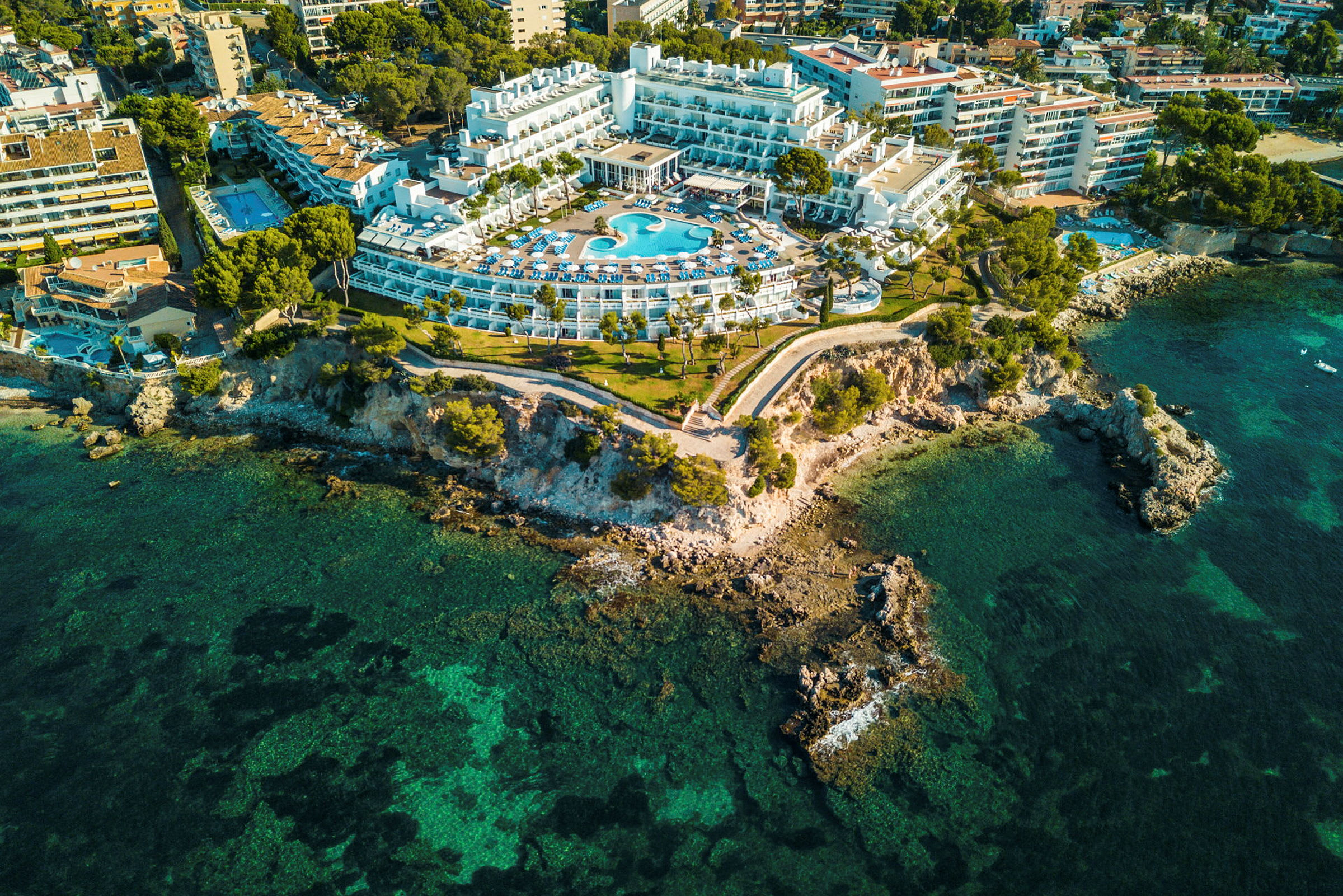 Flyfoto av et hotell med basseng, plassert ved en klippekyst. (AI-generert tekst)