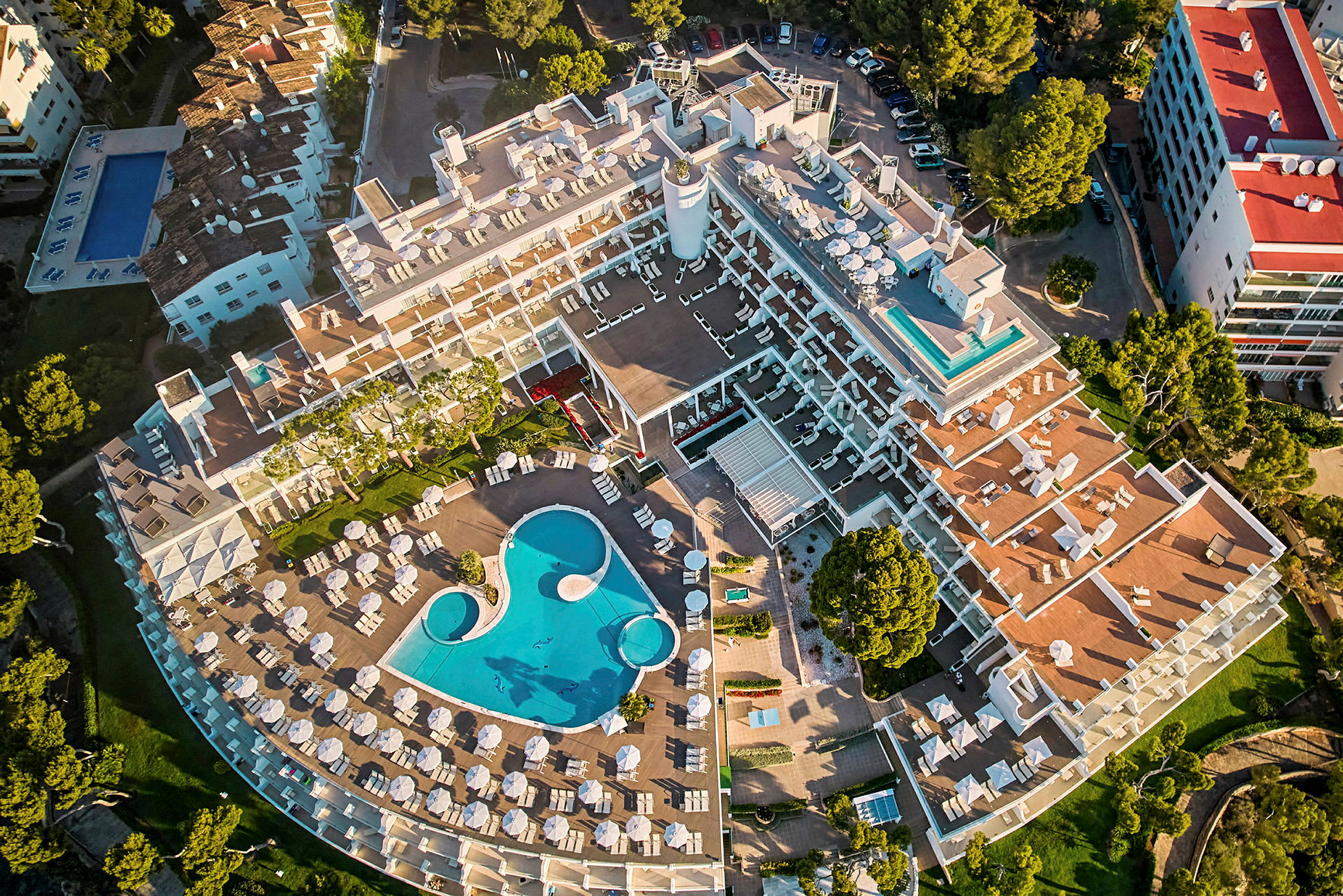 Luftfoto av en hotellbygning med utsikt over et bassengområde og solsenger. (AI-generert tekst)