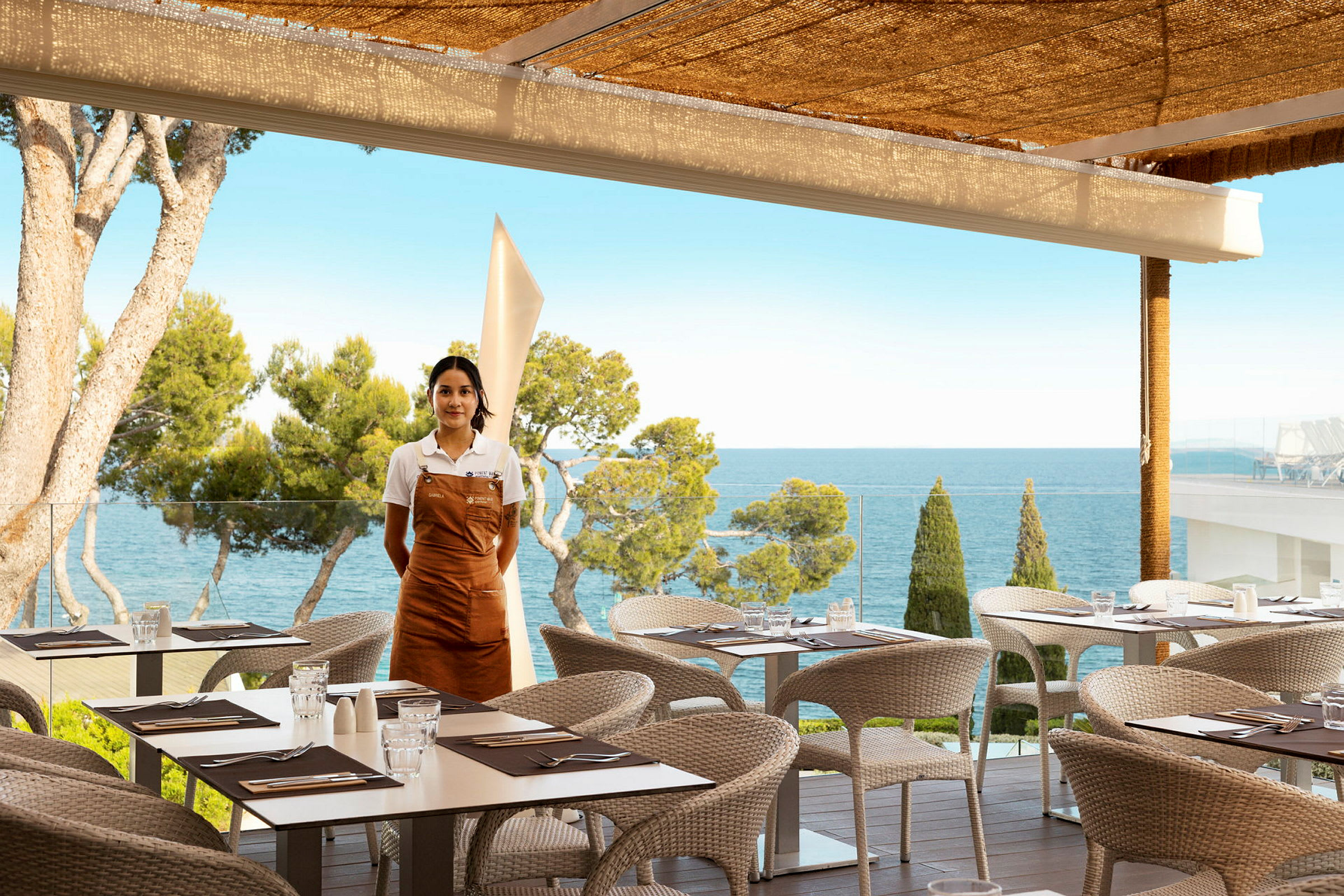 Restaurant med uteservering og havutsikt, en servitør står ved siden av. (AI-generert tekst)