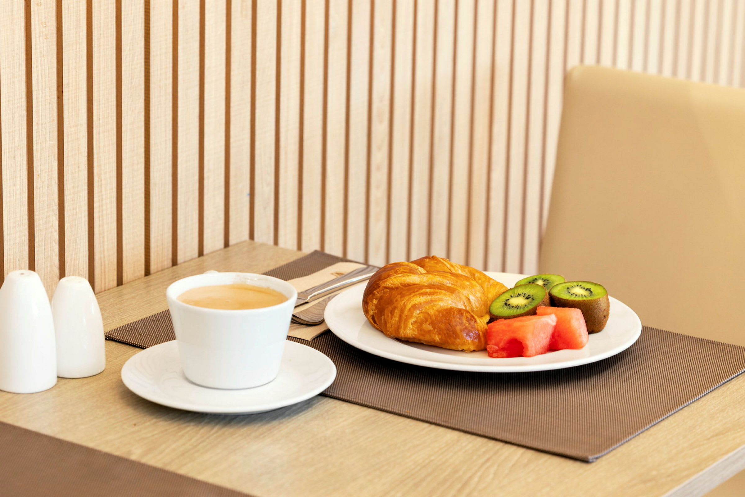 En frokost med kaffe, croissant og fersk frukt servert på bordet. (AI-generert tekst)