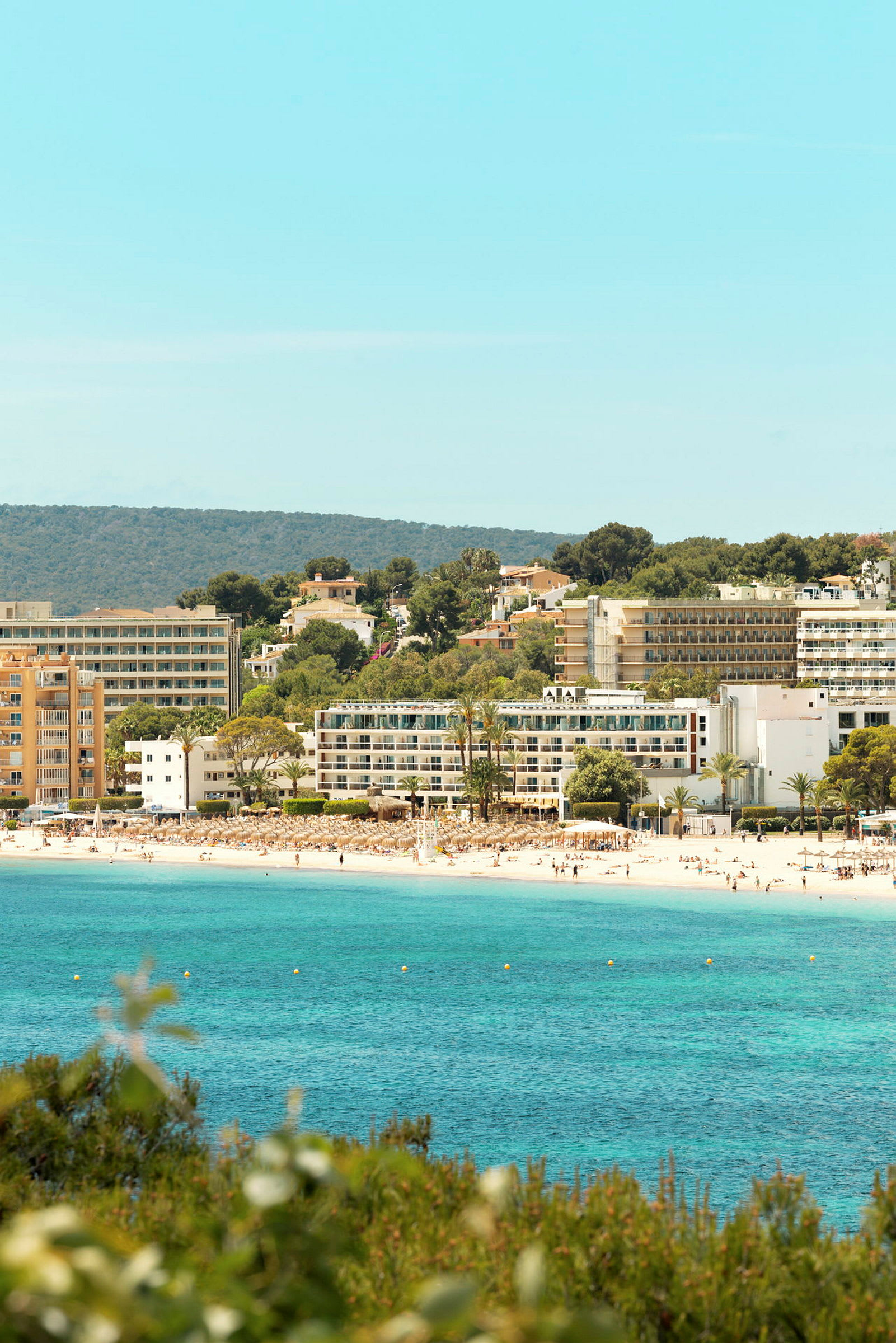 En strand med klart blått vann og hotellbygninger i bakgrunnen. (AI-generert tekst)