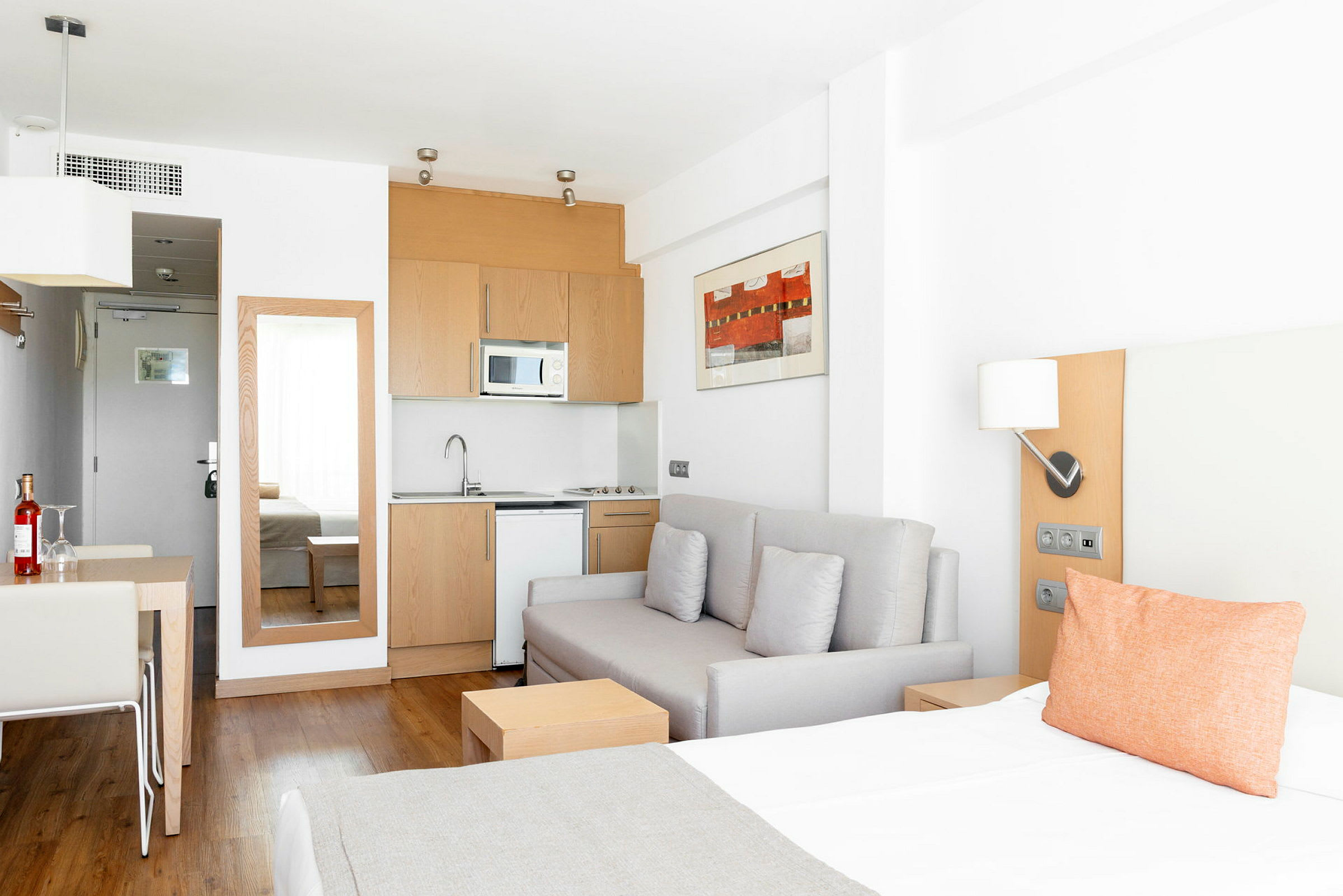 Et lyst hotellrom med en sovesofa, en kjøkkenkrok og et spisebord. (AI-generert tekst)