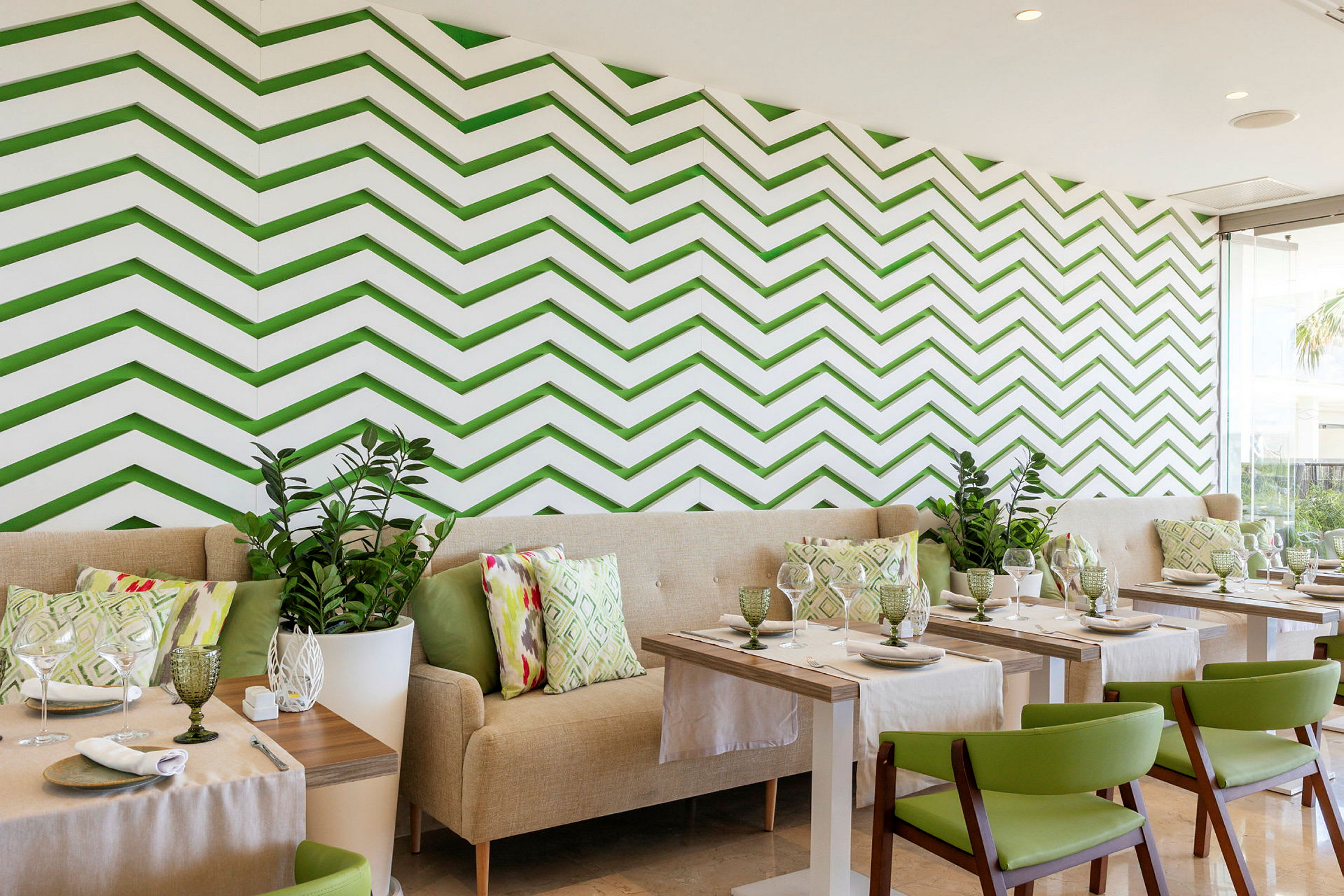 En restaurant med moderne interiør, grønne stoler, lyse sofaer og en vegg med grønn sikksakkmønster. (AI-generert tekst)
