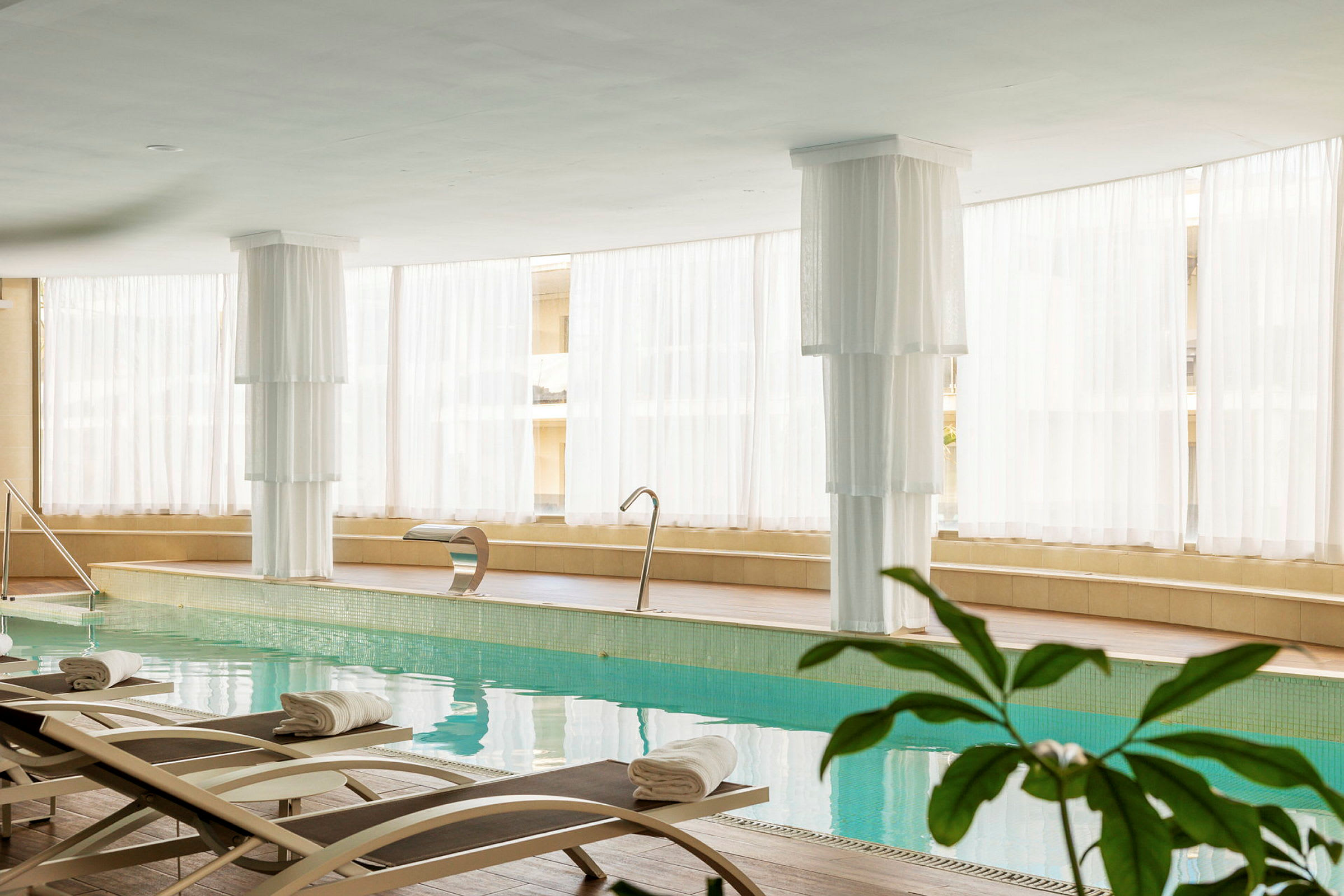 Interiør av et lyst spa med innendørsbasseng, solsenger og hvit innredning. (AI-generert tekst)