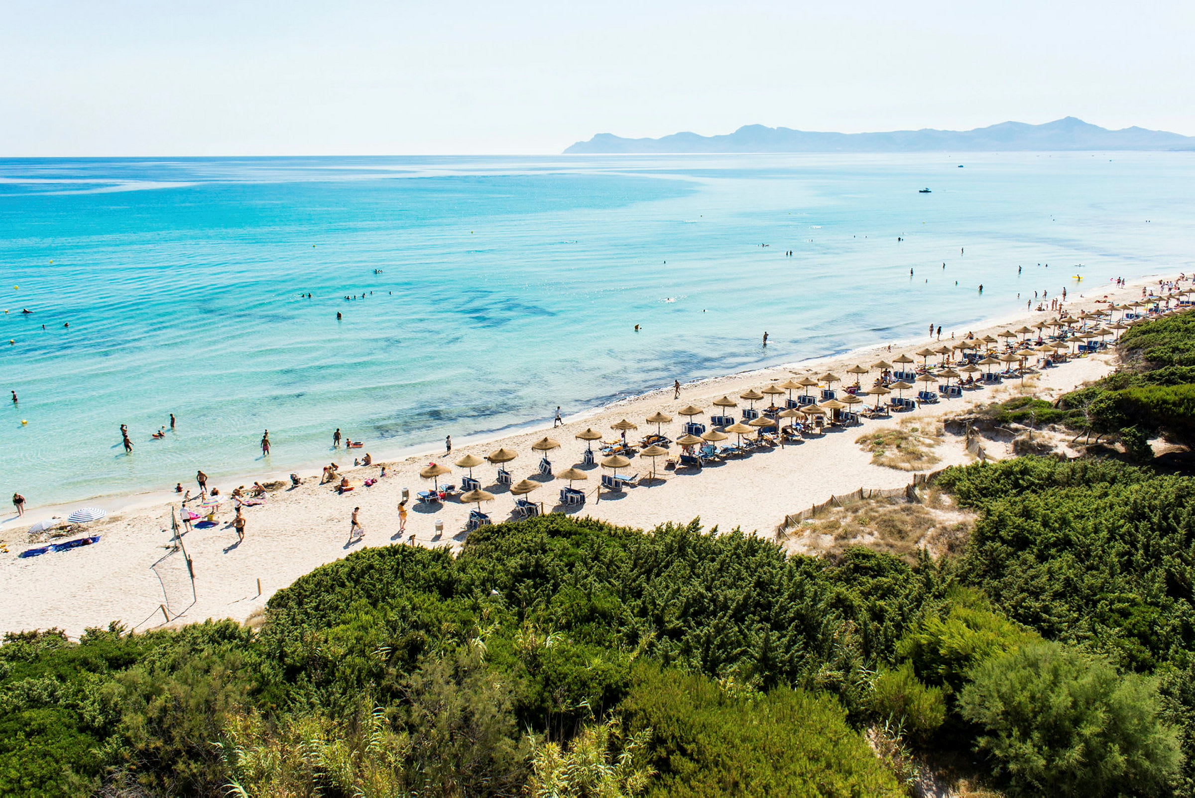 Strand med parasoller og solsenger nær klart blått vann. (AI-generert tekst)