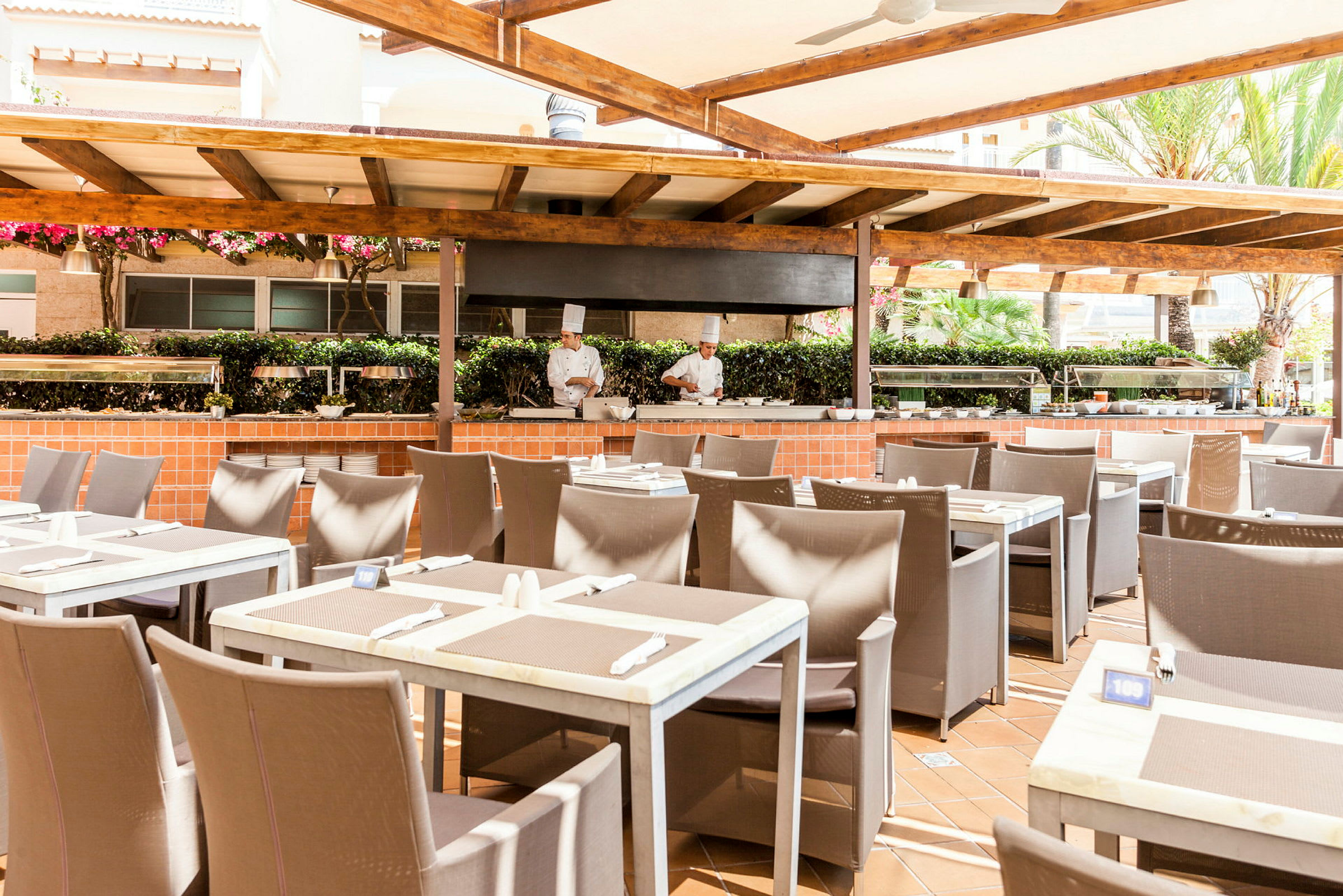 Utendørsrestaurant med dekkede bord og matlagingsstasjon under en trepergola. (AI-generert tekst)