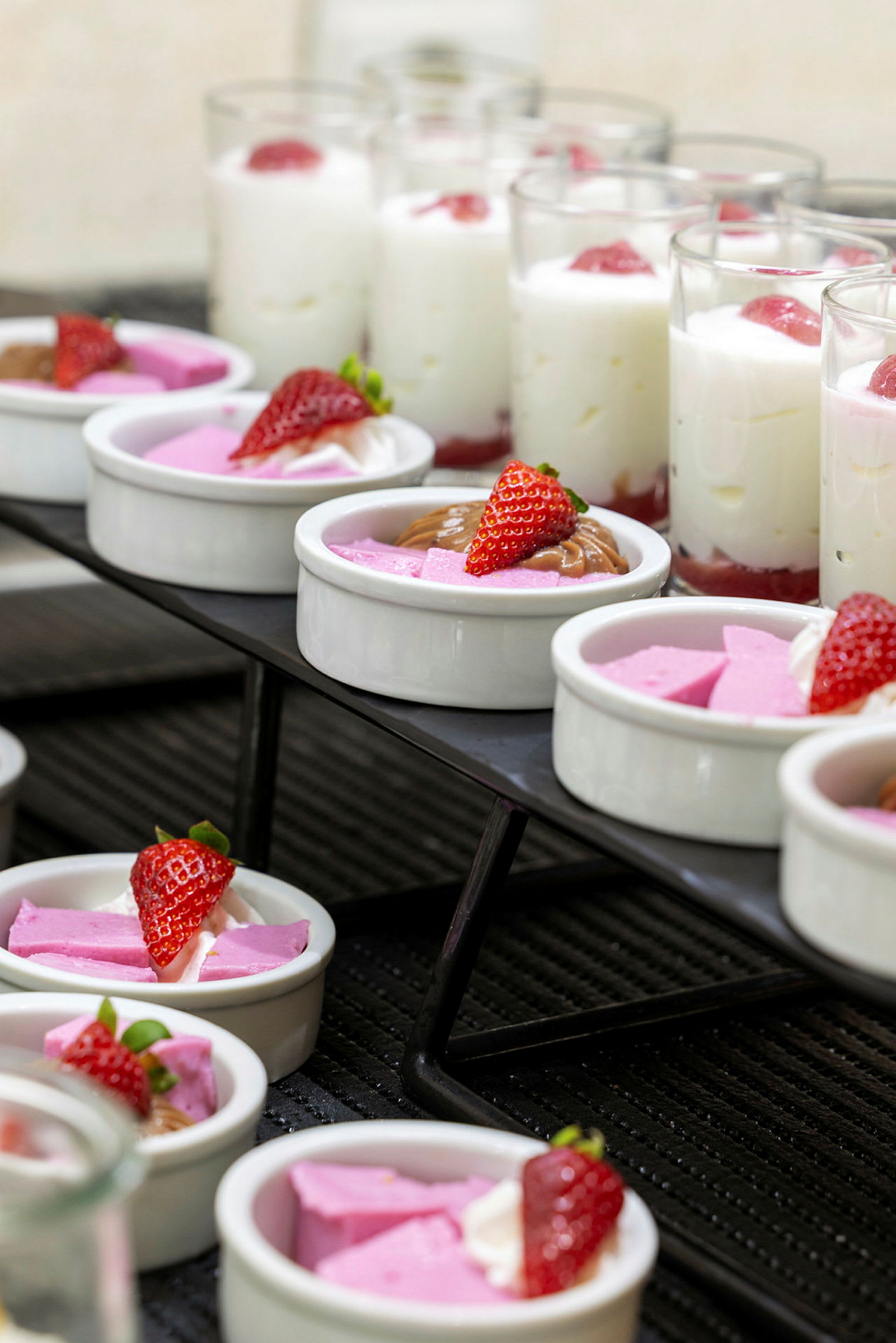 Et utvalg av desserter, inkludert skåler med rosa mousse og jordbær samt glass med hvit mousse og jordbær. (AI-generert tekst)
