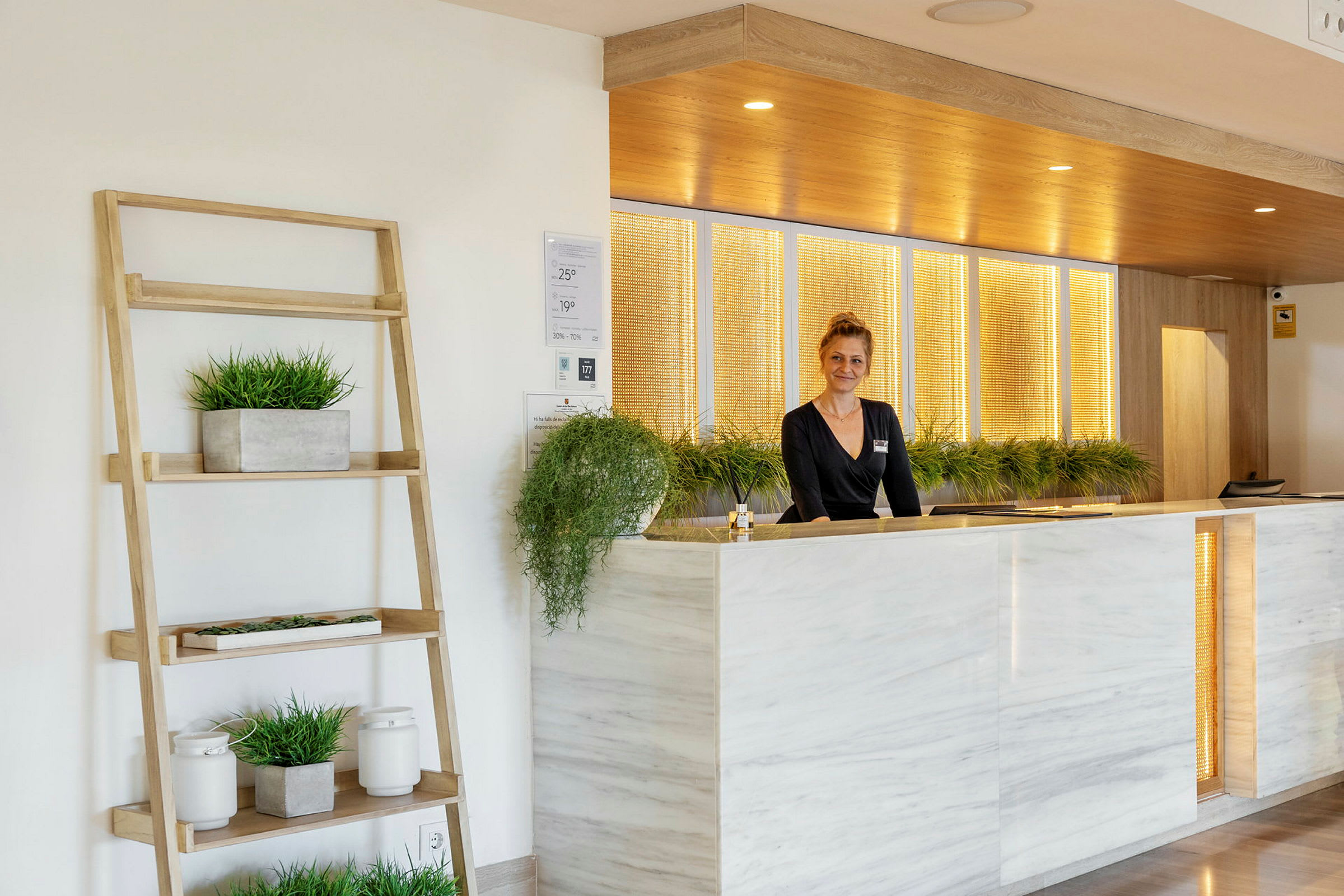 Resepsjon med marmorpanel og planter. En person står bak disken. (AI-generert tekst)