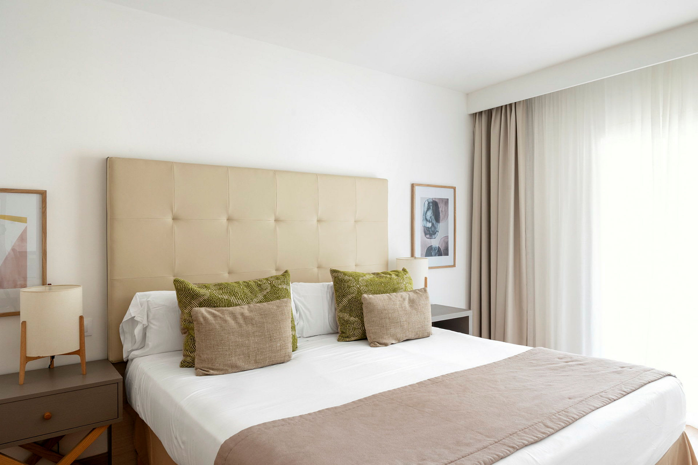 Et lyst og elegant hotellrom med en ferdig oppredd seng. Gardiner til høyre og nattbord til venstre. (AI-generert tekst)