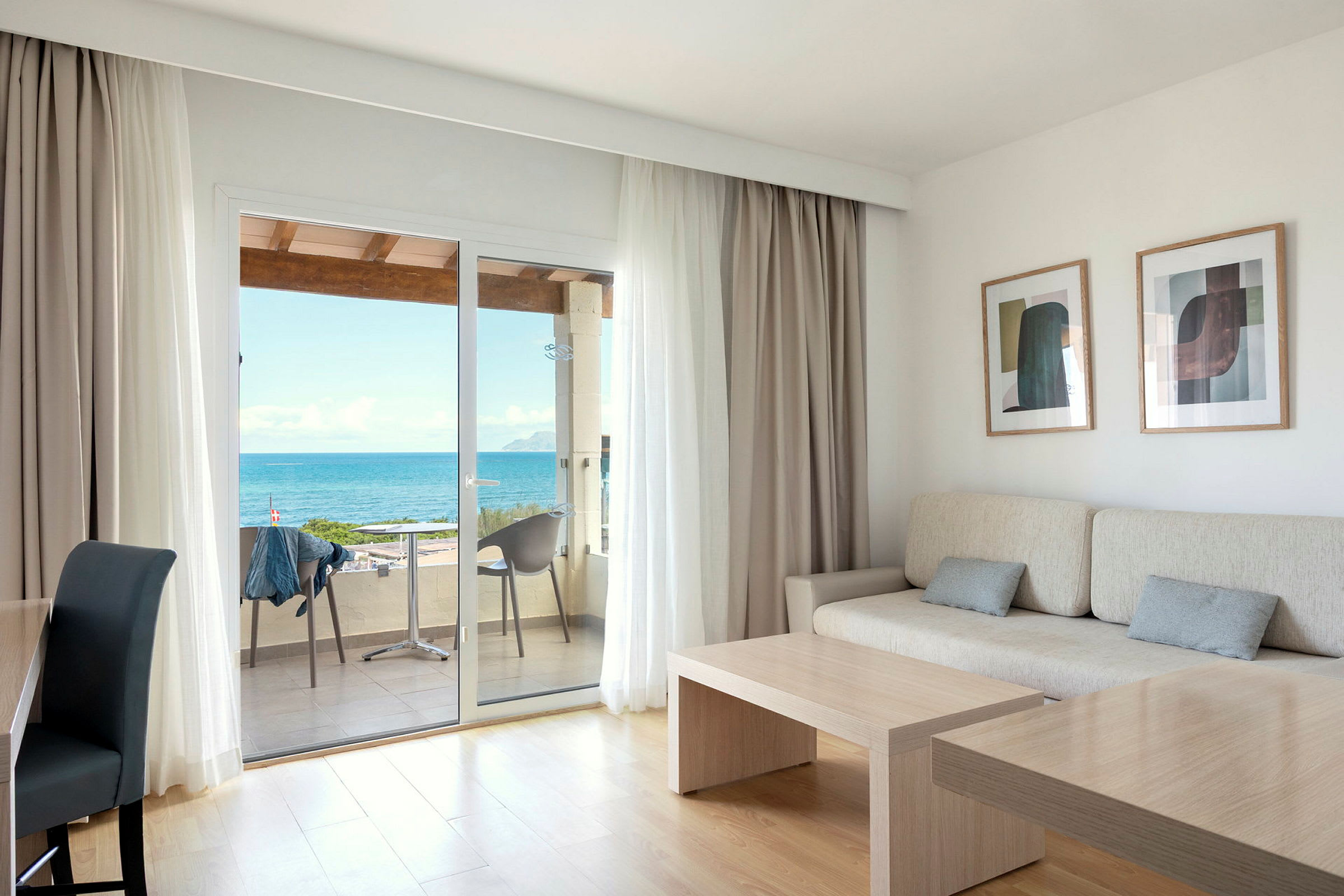 Et lyst rom med sofa, bord og store glassdører som leder til en balkong med utsikt over havet. (AI-generert tekst)