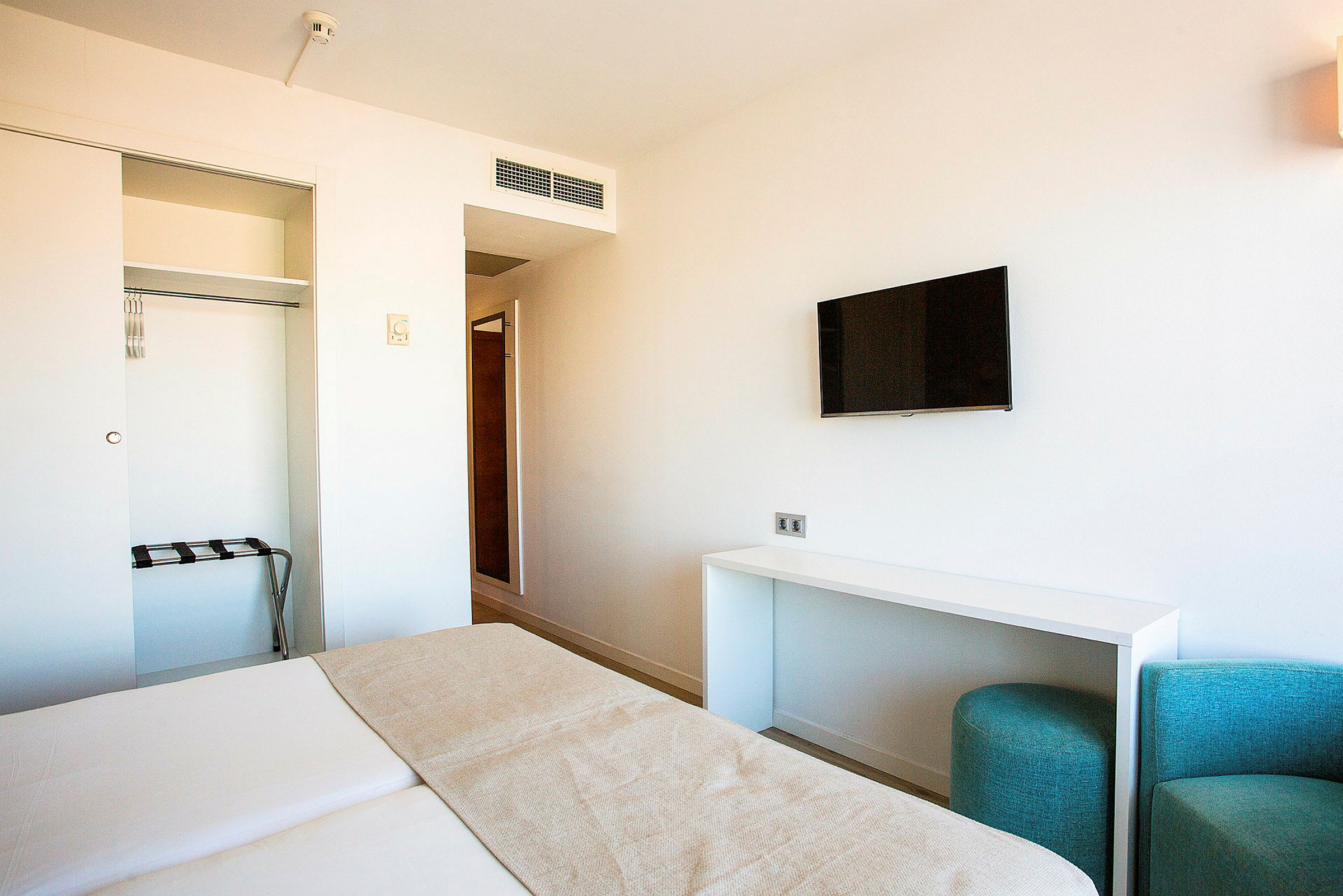 Et moderne hotellrom med en seng, en veggmontert TV og en åpen garderobe. (AI-generert tekst)