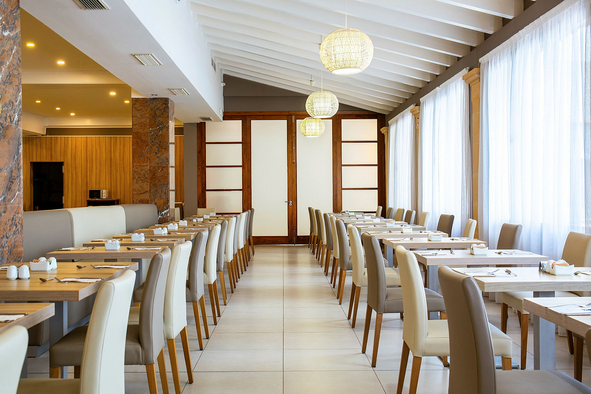 Interiør av en lys restaurant med dekkede bord og stoler. (AI-generert tekst)