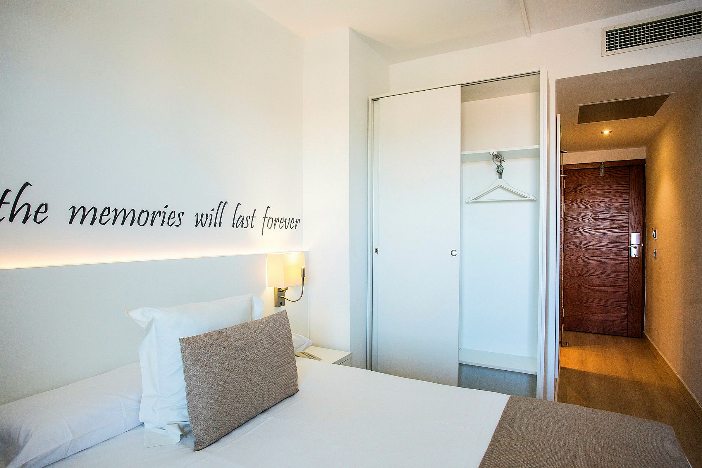 Et hotellrom med en seng, garderobe og inngangsdør. (AI-generert tekst)