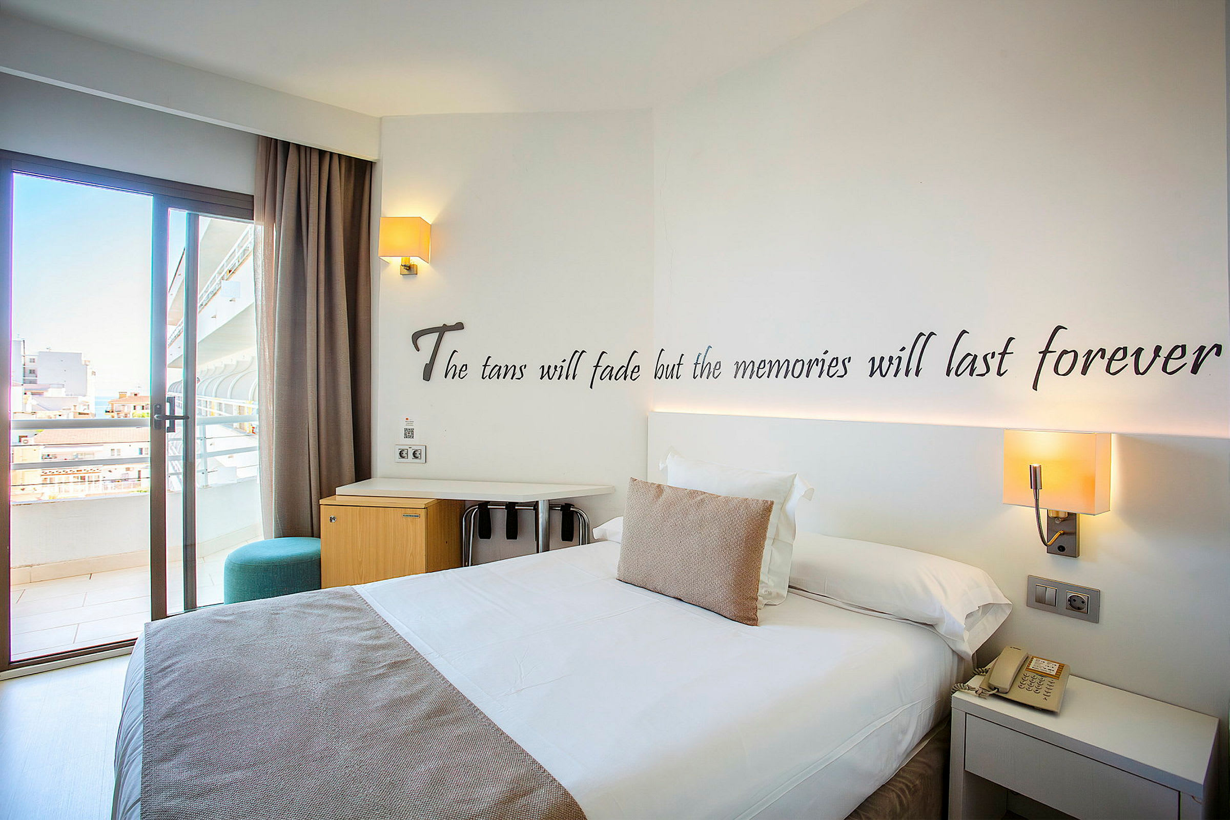 Hotellrom med en dobbeltseng, skrivebord og balkongdør. (AI-generert tekst)