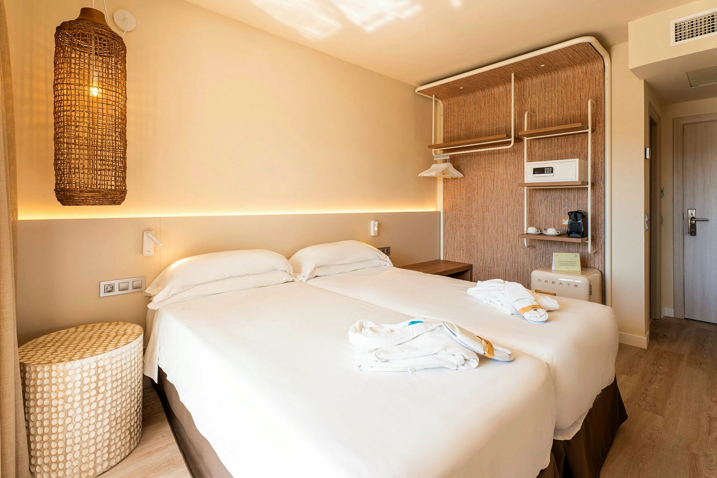 Et hotellrom med en dobbeltseng, lys innredning og en flettet lampe som henger på veggen. (AI-generert tekst)