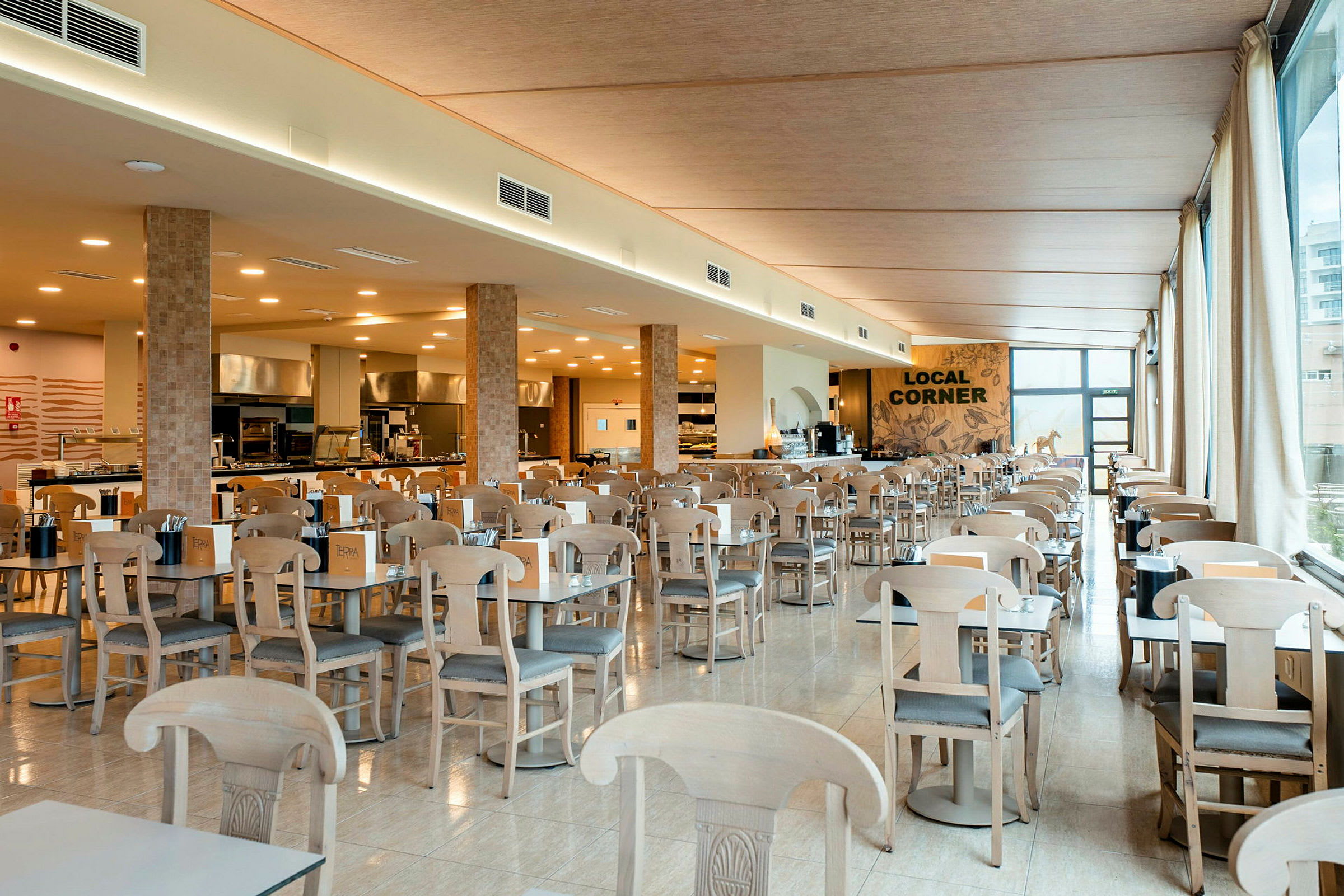 Interiør av en romslig restaurant med mange bord og stoler samt en serveringsdisk i bakgrunnen. (AI-generert tekst)