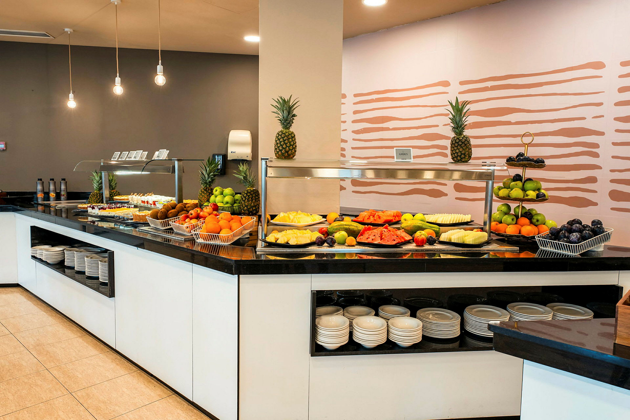 Bilde av en buffetdisk med frisk frukt og mat oppstilt, under moderne taklamper. (AI-generert tekst)