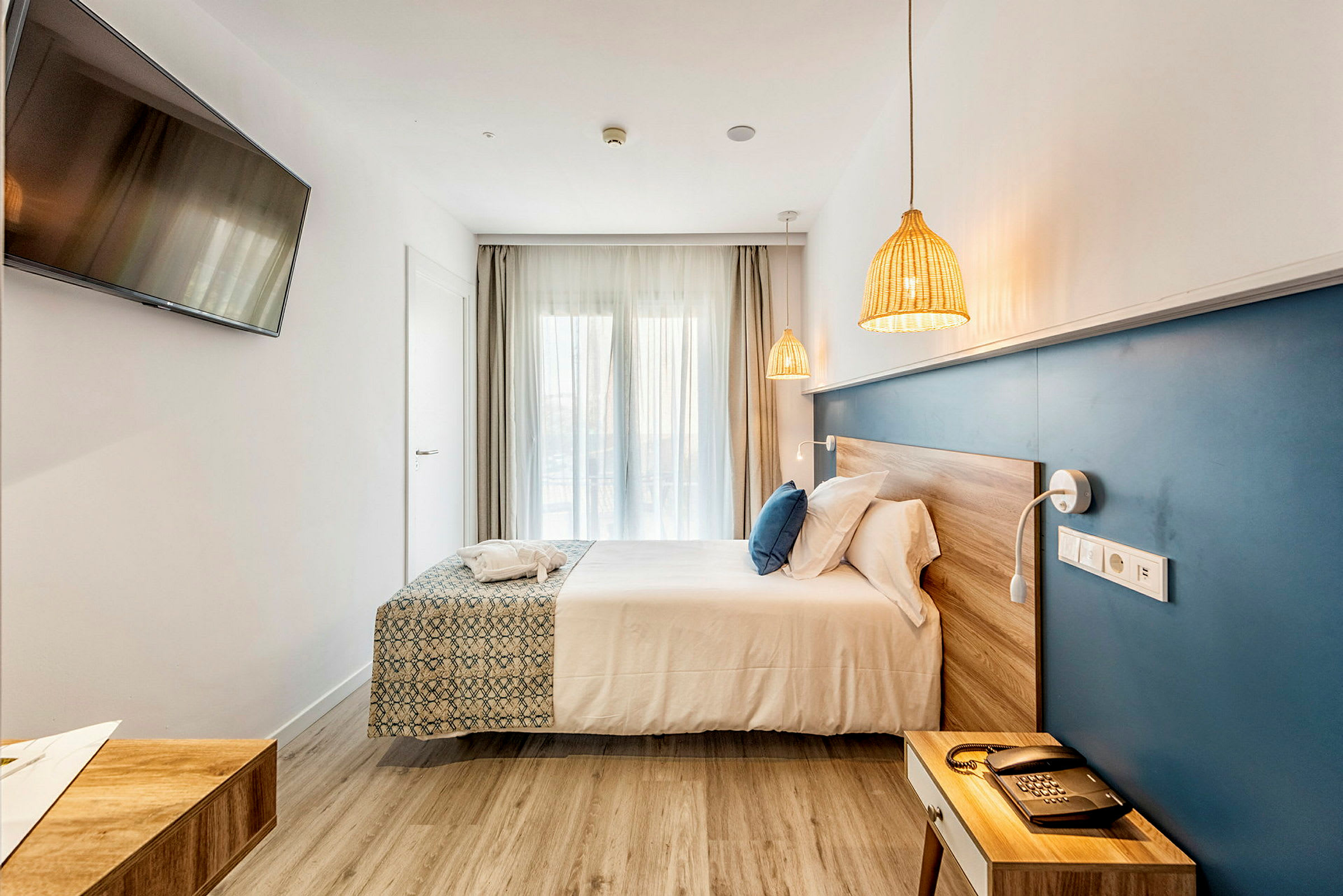 Et hotellrom med en dobbeltseng, en blå veggpanel, en TV på veggen og naturlige treoverflater. (AI-generert tekst)