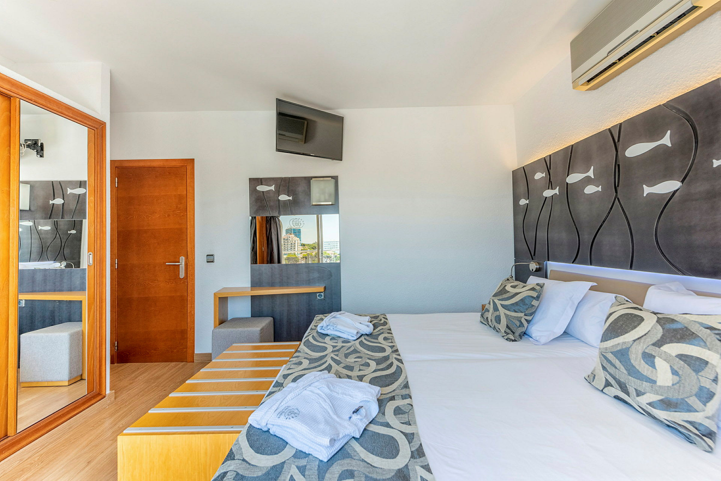 Et hotellrom med en dobbeltseng, dekorative fisker på sengegavlen og et skrivebord med et speil. (AI-generert tekst)