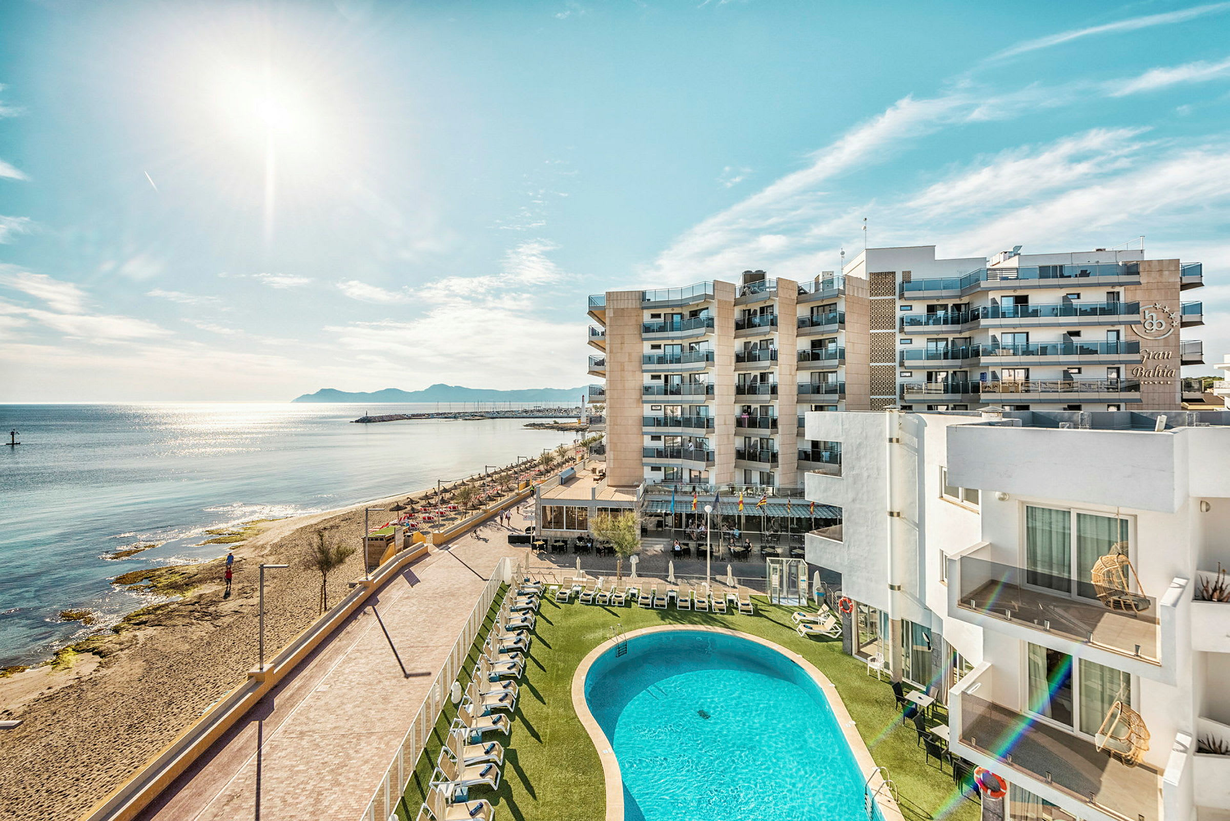 Hotellbyggnader ved stranden med bassengområde og hav i bakgrunnen. (AI-generert tekst)