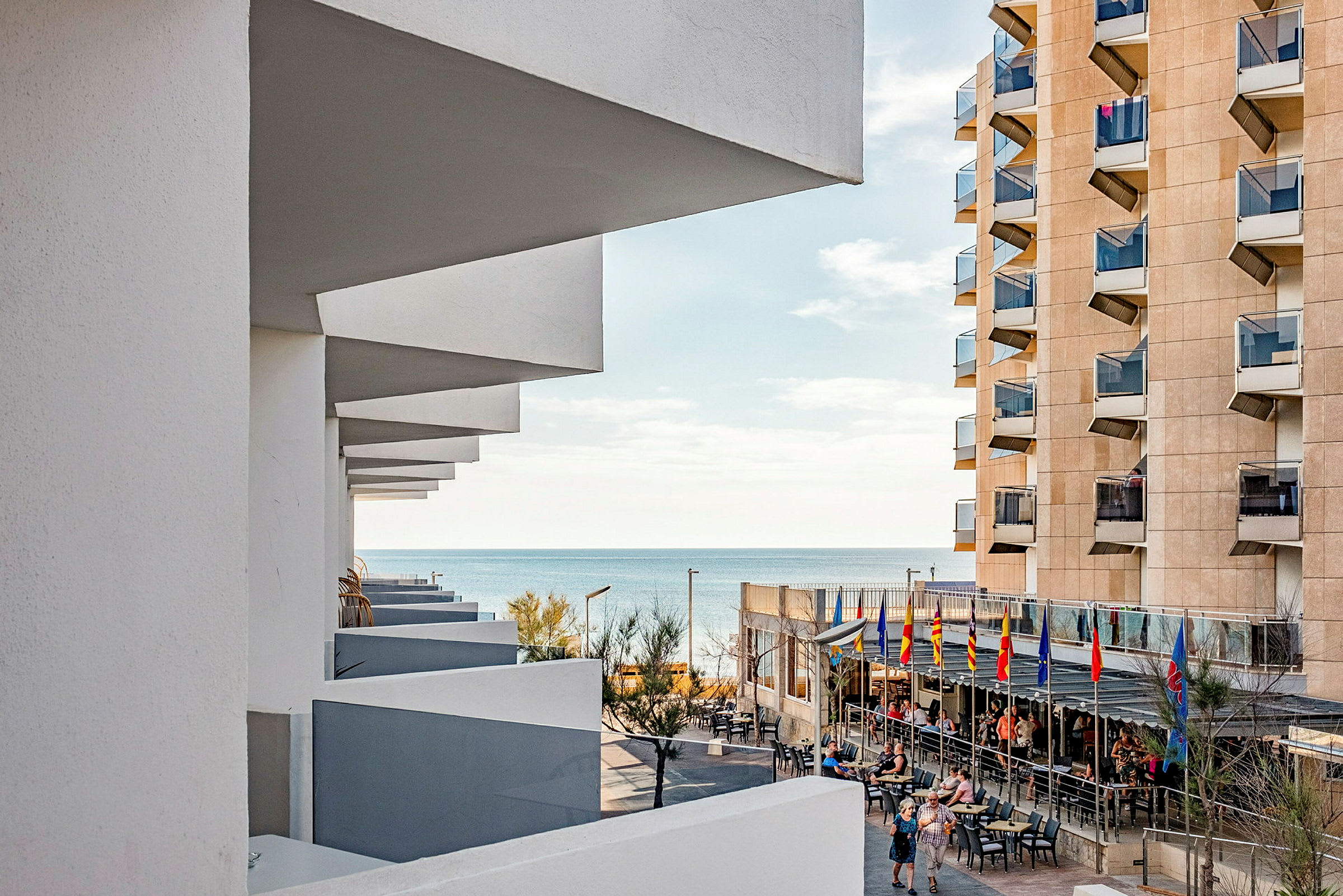 En utsikt over havet sett fra et hotell med terrasse og balkonger på bygningen. (AI-generert tekst)