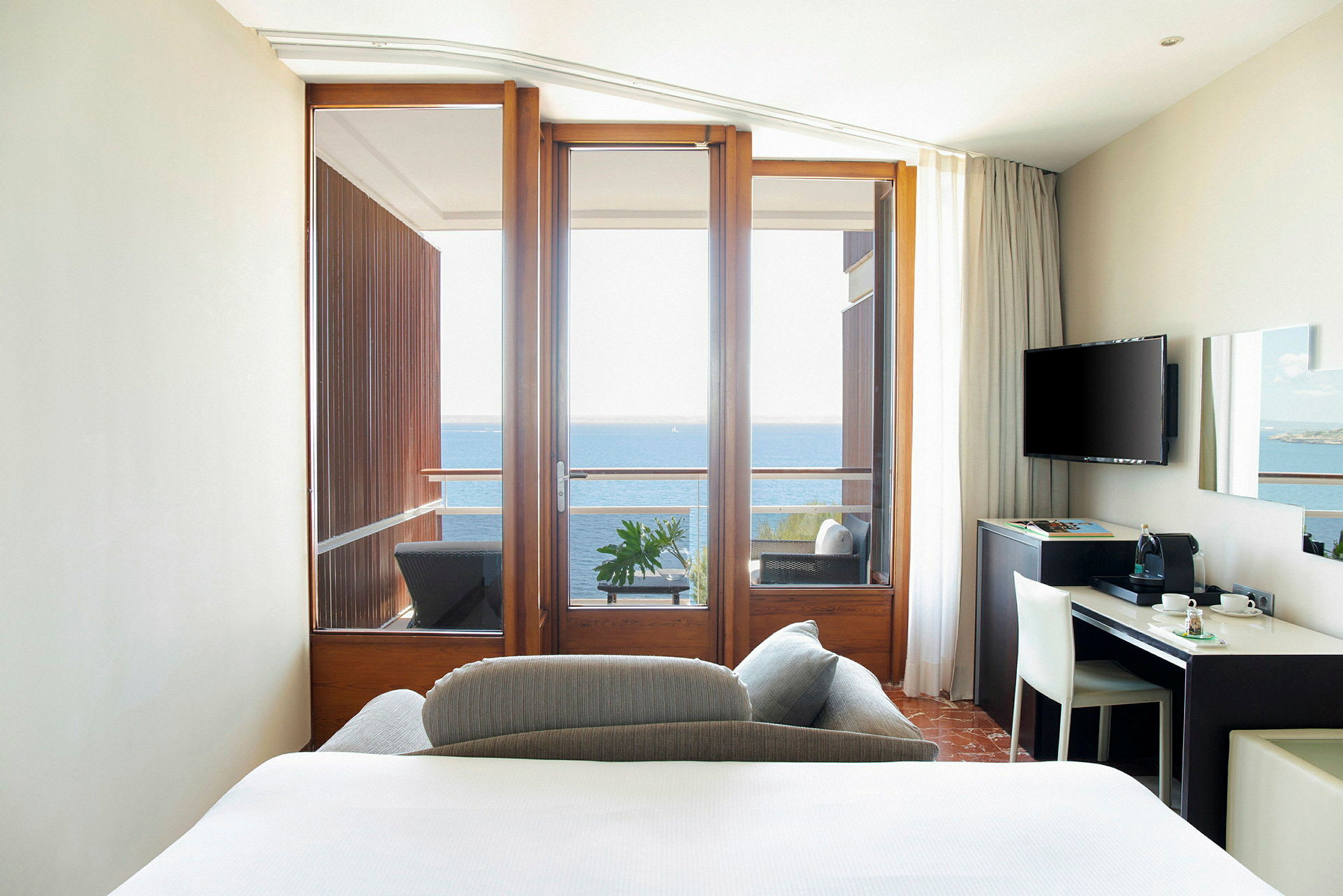 Hotellrom med balkong mot havet og en enkel arbeidsstasjon. (AI-generert tekst)