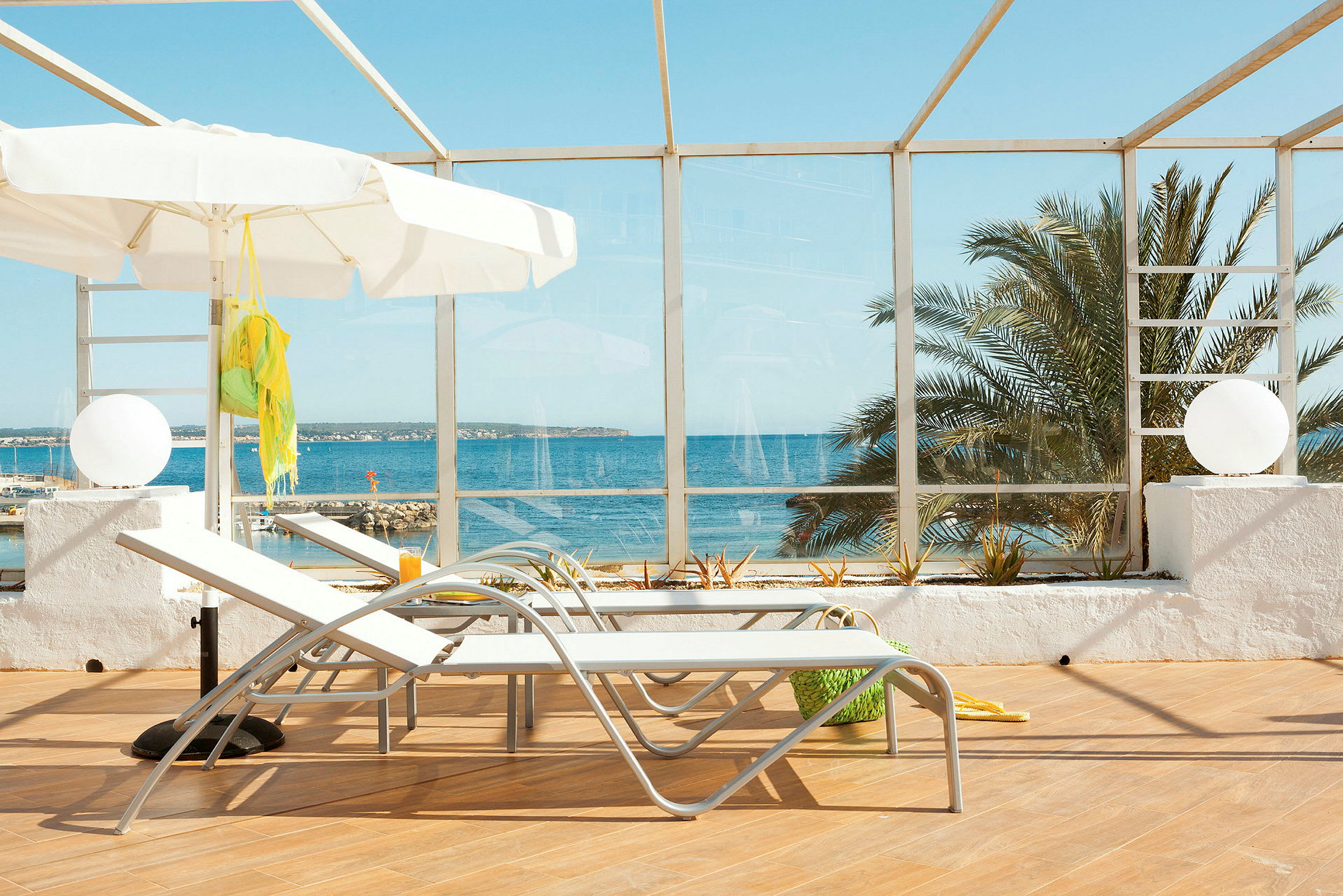 To solsenger og en hvit parasoll på en terrasse med utsikt over havet. (AI-generert tekst)