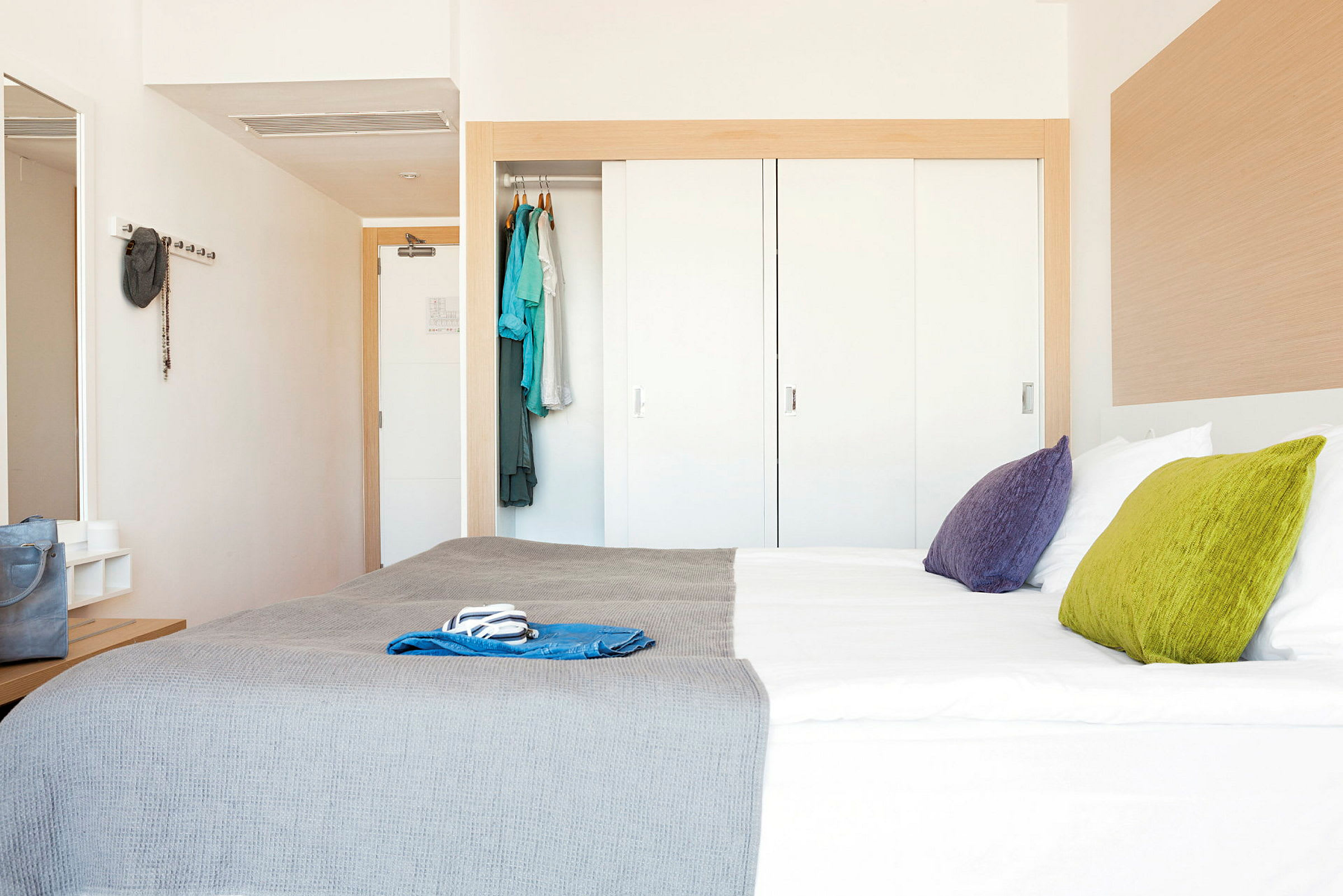 Et hotellrom med en dobbeltseng, fargerike puter og en garderobe. (AI-generert tekst)