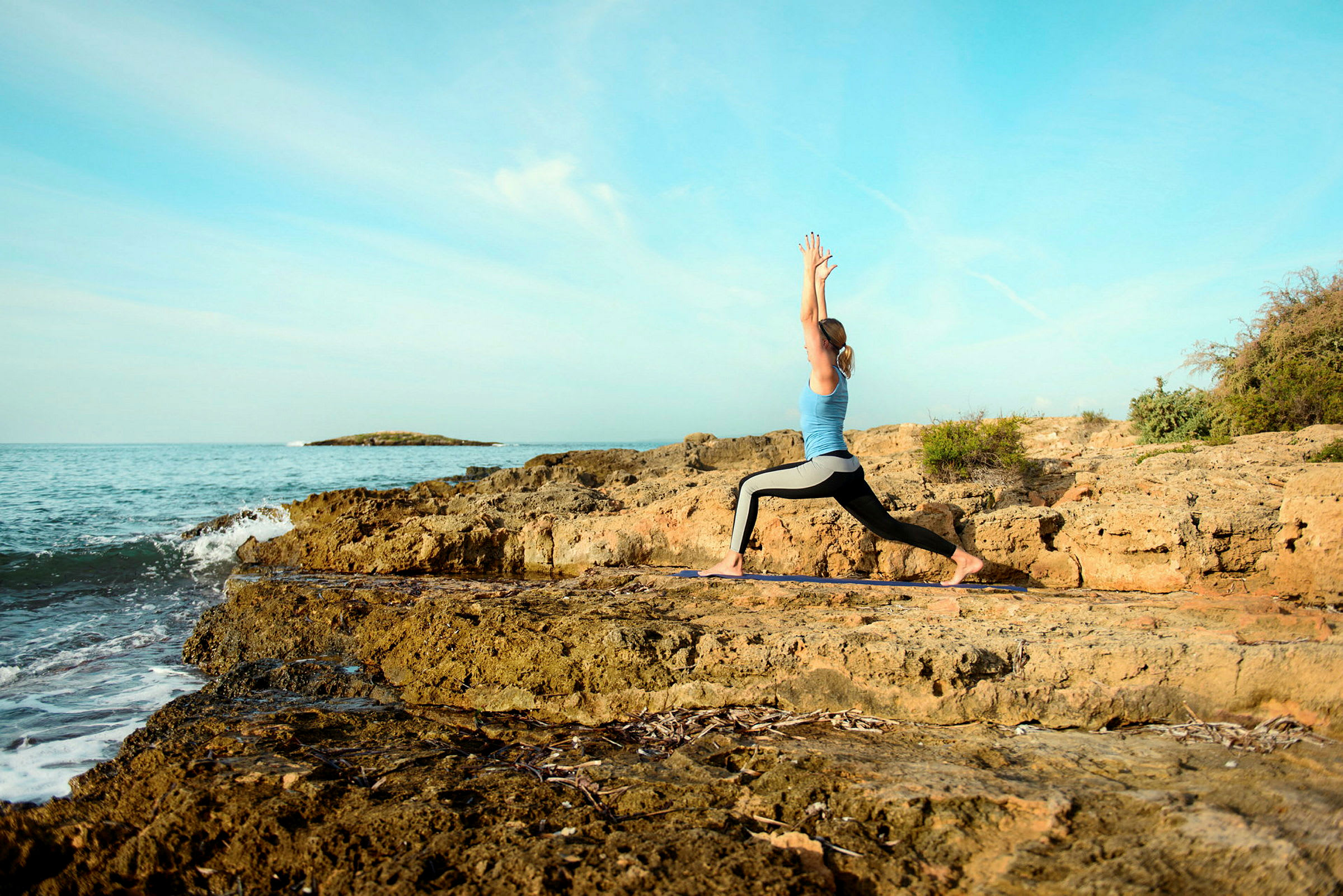 Person utfører yogaøvelse på steinete kyst ved havet. (AI-generert tekst)