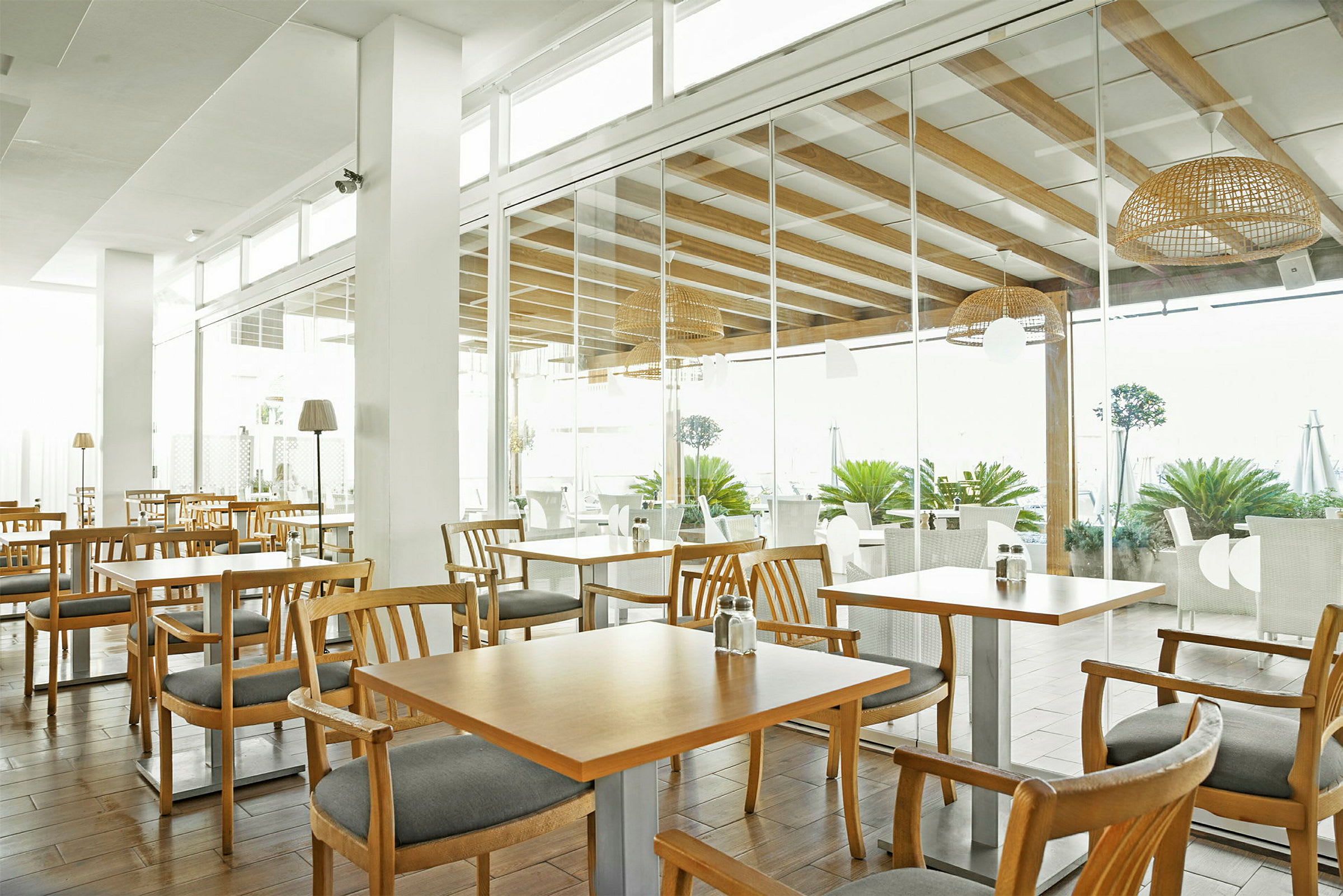 En restaurant med trebord og stoler, lyse interiører og store glassvegger. (AI-generert tekst)