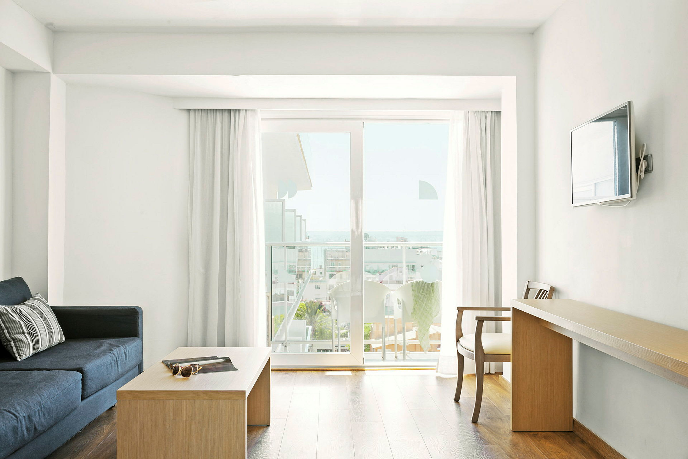 Et hotellrom med salongbord, sofa, skrivebord og balkong med utsikt. (AI-generert tekst)