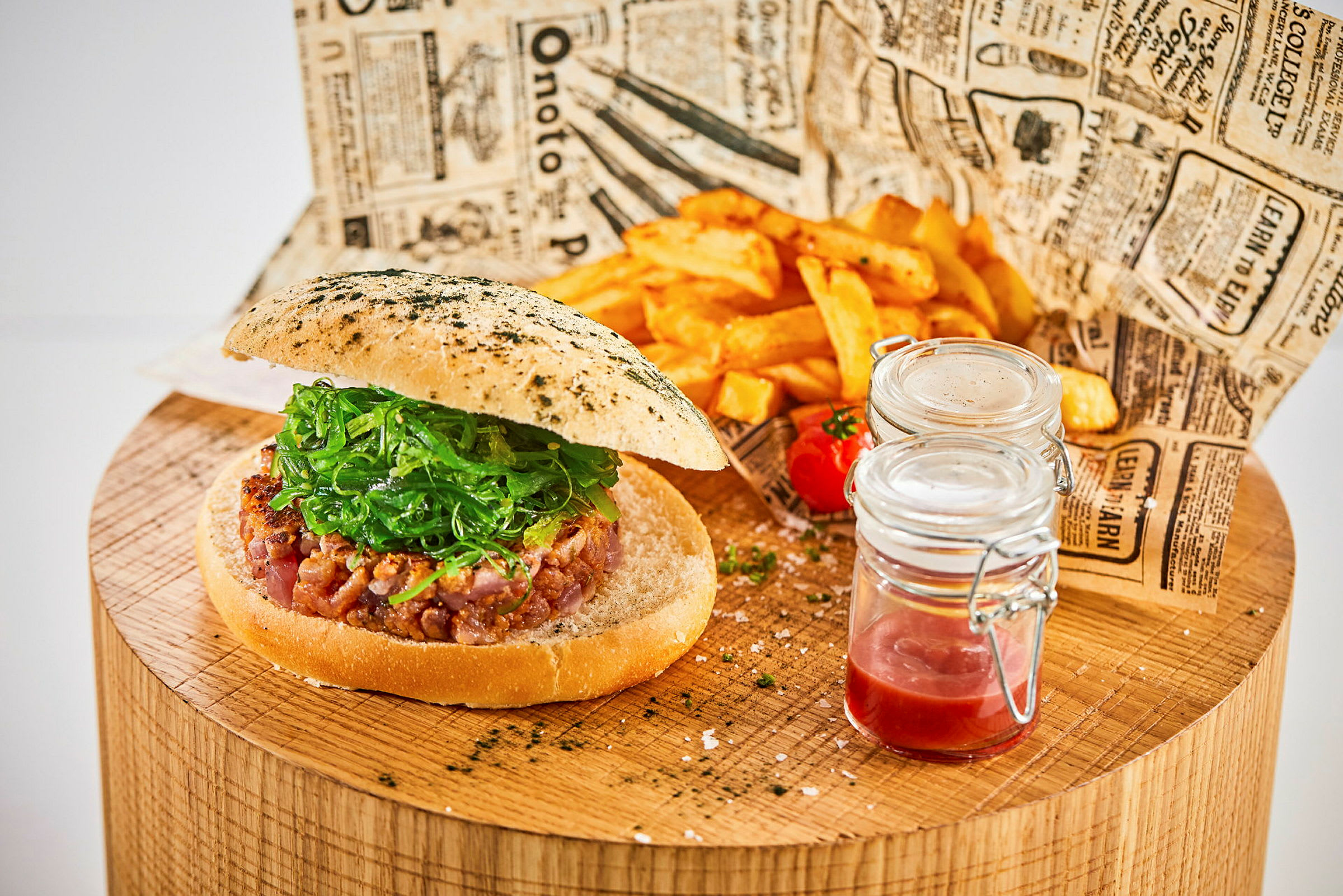 En hamburger med salat på et trebord sammen med pommes frites og glasskrukker med saus. (AI-generert tekst)
