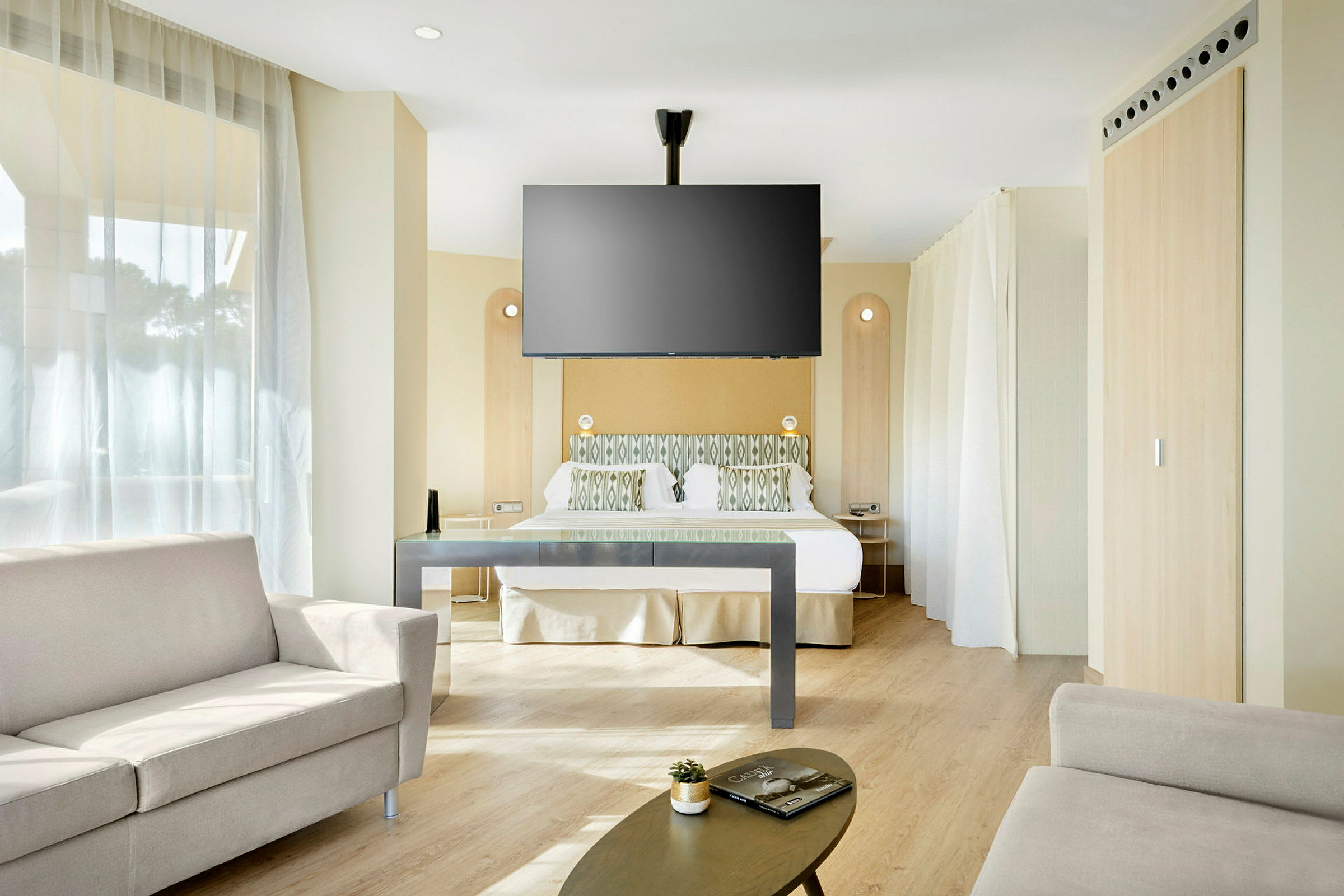 Et hotellrom med seng, sofa og veggmontert TV. (AI-generert tekst)