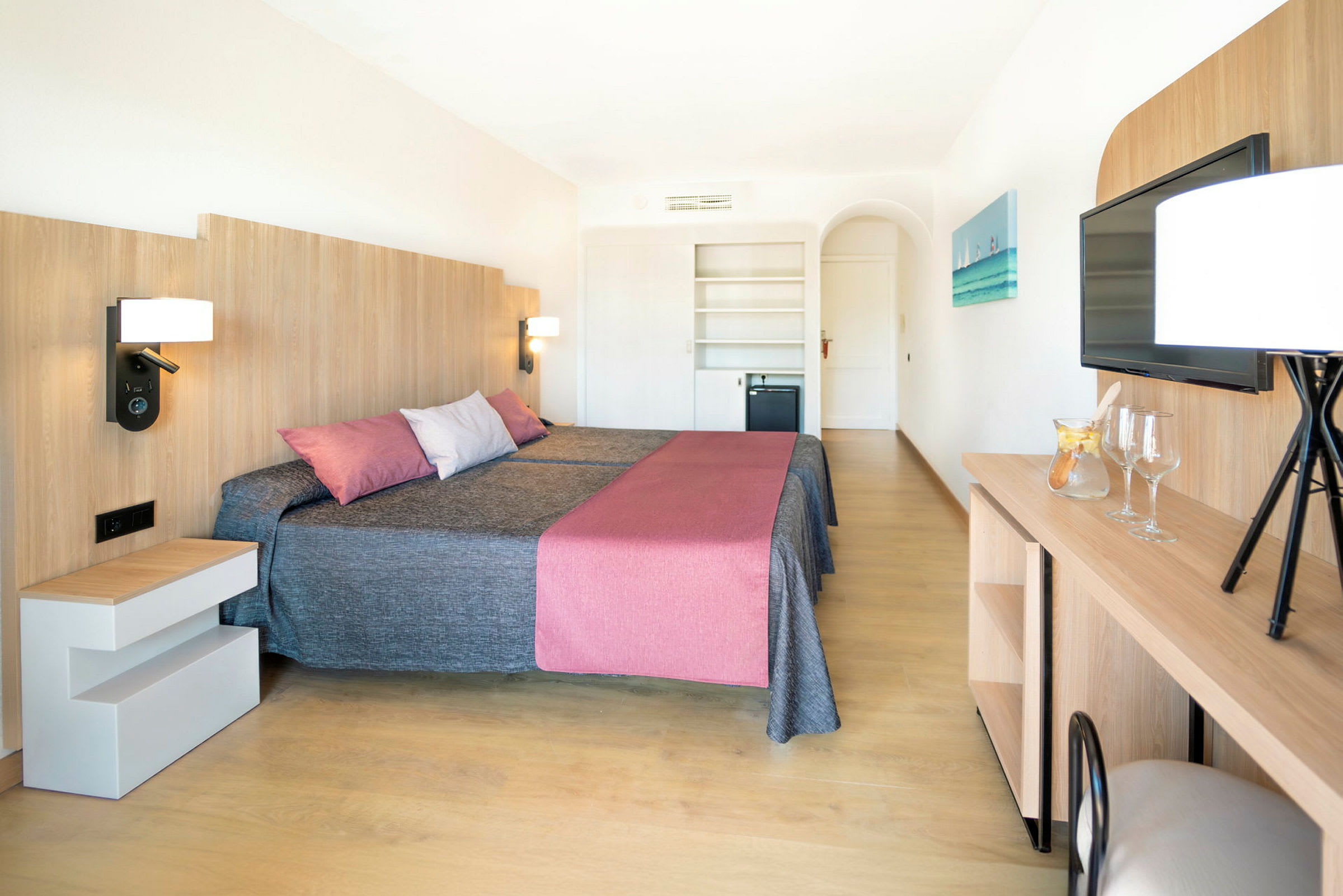 Et hotellrom med to senger, en moderne innredning med tredetaljer, og en TV på veggen. (AI-generert tekst)