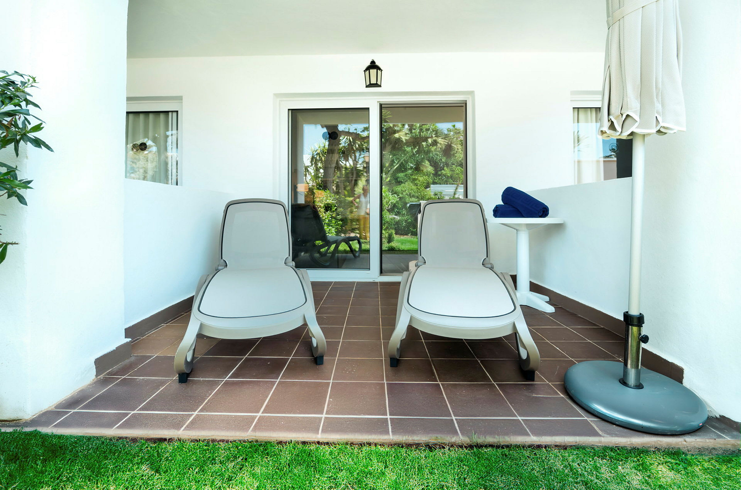 To solsenger på en terrasse ved et hotellrom, med et bord og en sammenfoldet parasoll. (AI-generert tekst)