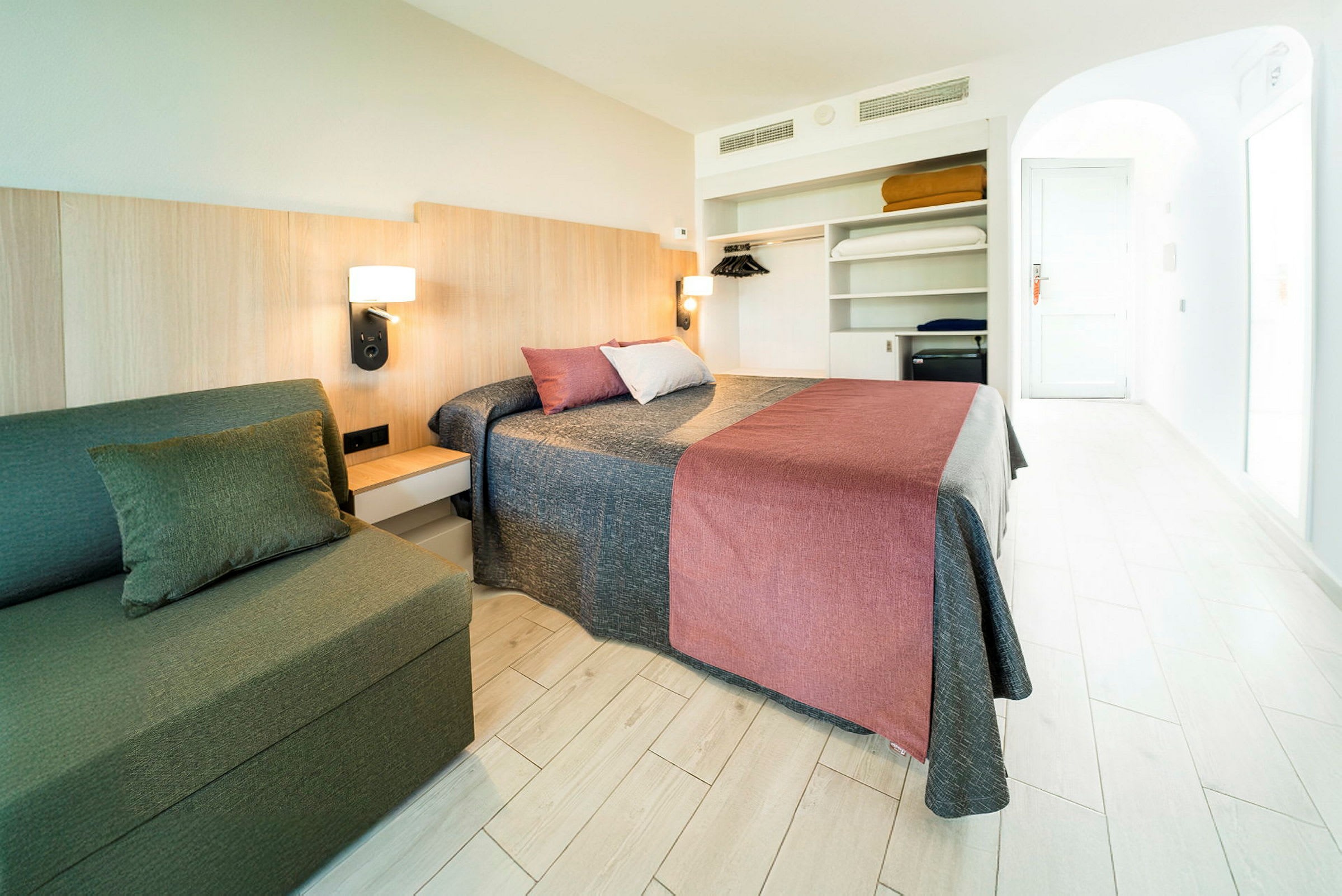 Et hotellrom med dobbeltseng, sofa og åpen garderobe. (AI-generert tekst)