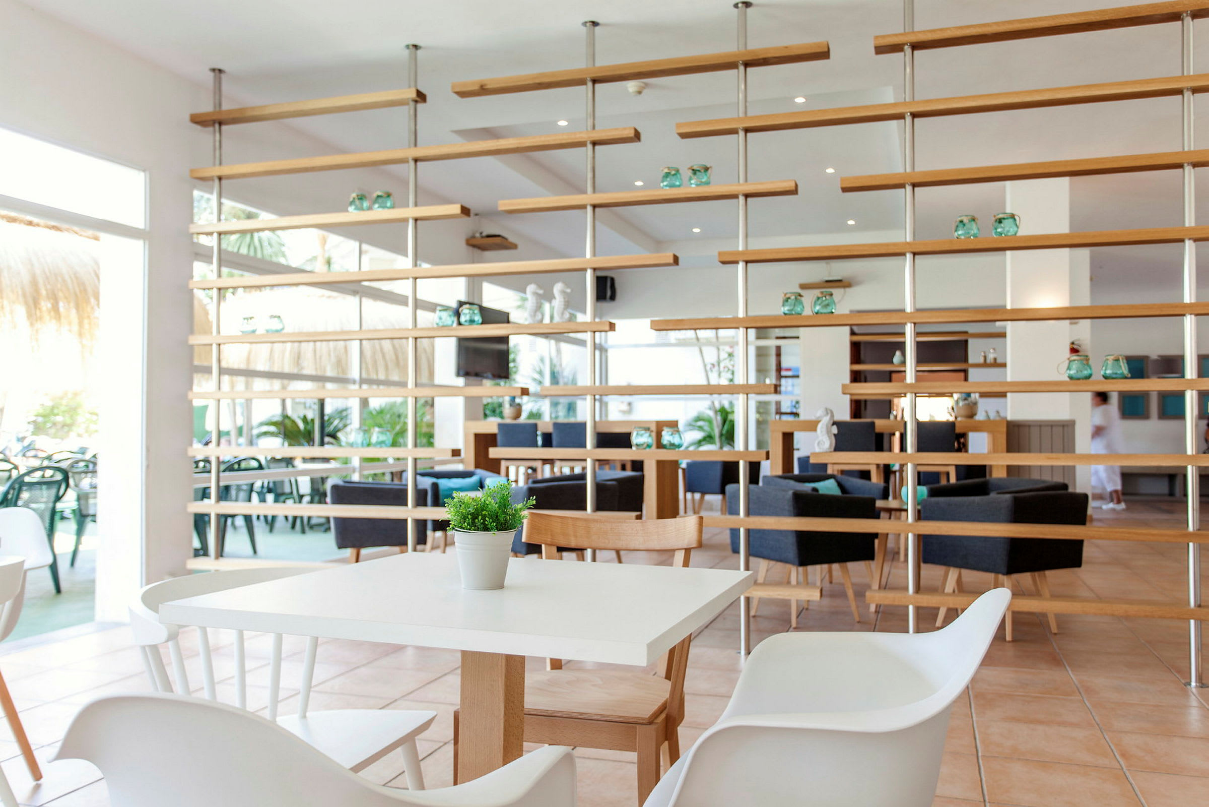 En lys og moderne restaurant med hvite bord, trestoler og dekorative hyller. (AI-generert tekst)