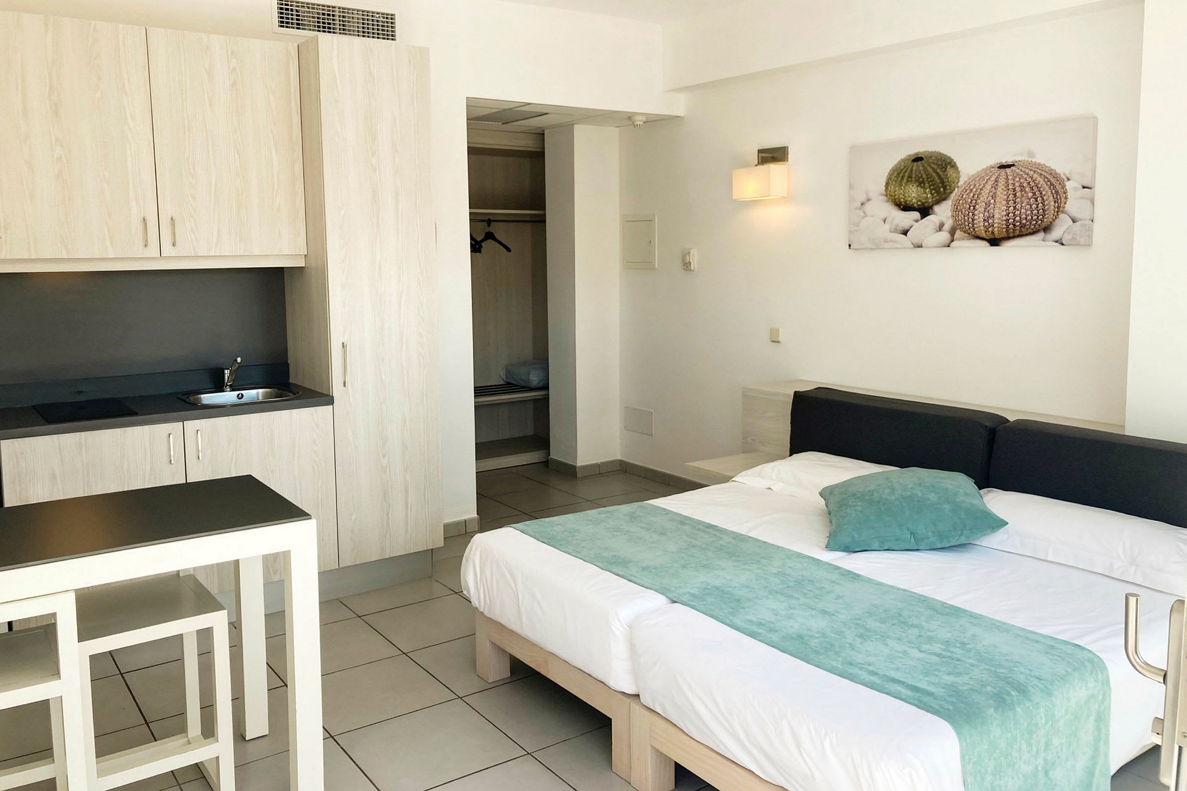 Bilde av et hotellrom med en seng, et lite kjøkken og en garderobe. (AI-generert tekst)